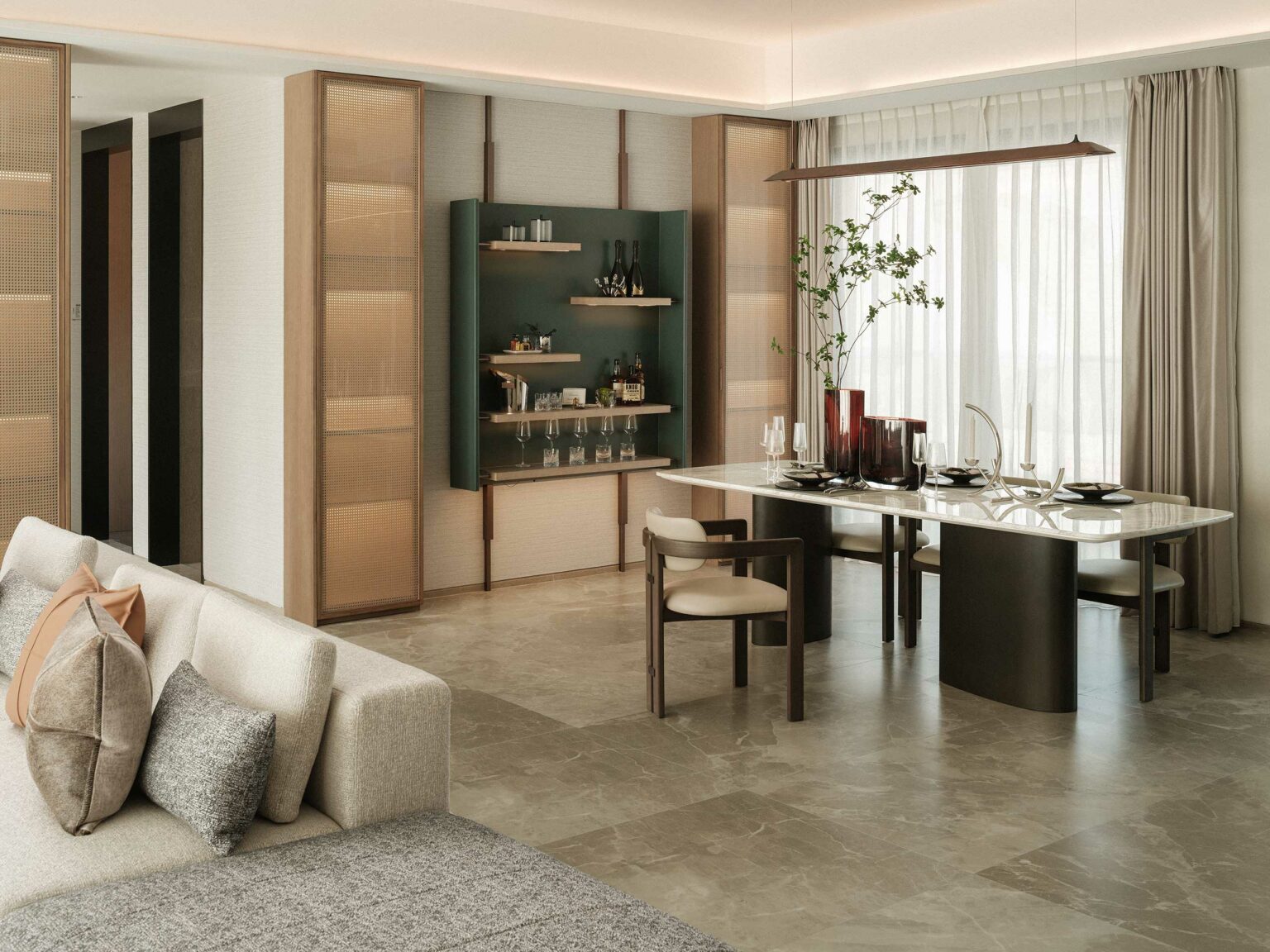 A modern dining area features a sleek marble table with six chairs, set with dark tableware. A cozy beige sofa with gray pillows is nearby. A sideboard with glassware and decor sits against the wall. Light filters through sheer curtains, adding a serene ambiance.