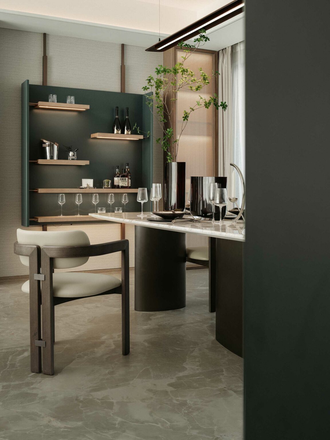 Modern dining room with elegant design. Features a marble table, sleek wooden chair, wall shelves with glassware, and a tall plant, conveying a serene, sophisticated atmosphere.