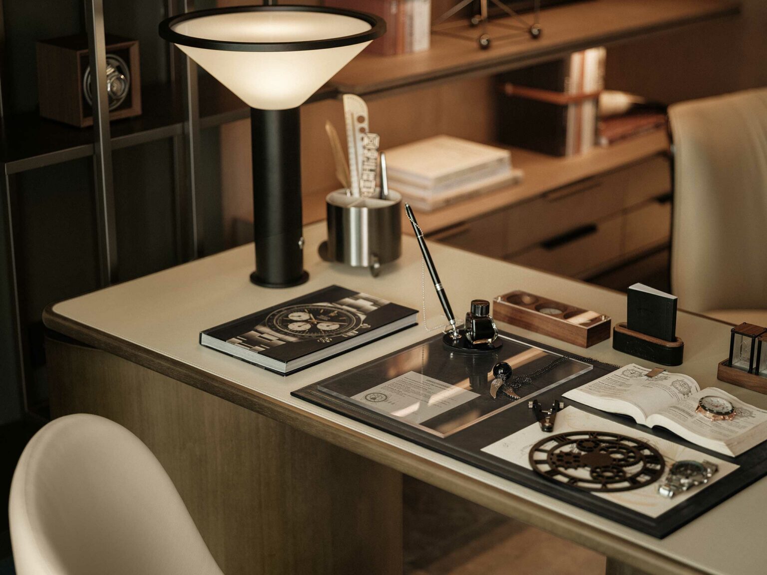 Cozy study desk scene with a modern lamp, open journal, watch parts, fountain pen, and elegant decor, conveying a studious, refined atmosphere.