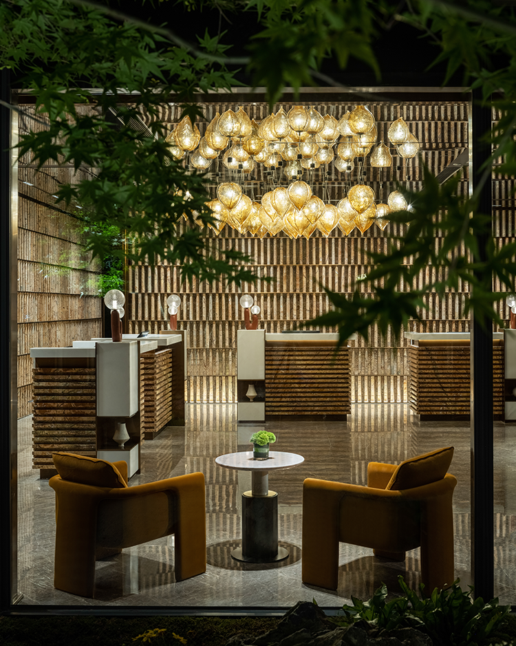 Elegant interior with soft lighting from clustered pendant lights reflecting on polished floors. Two mustard armchairs and a small table suggest a cozy, inviting atmosphere.
