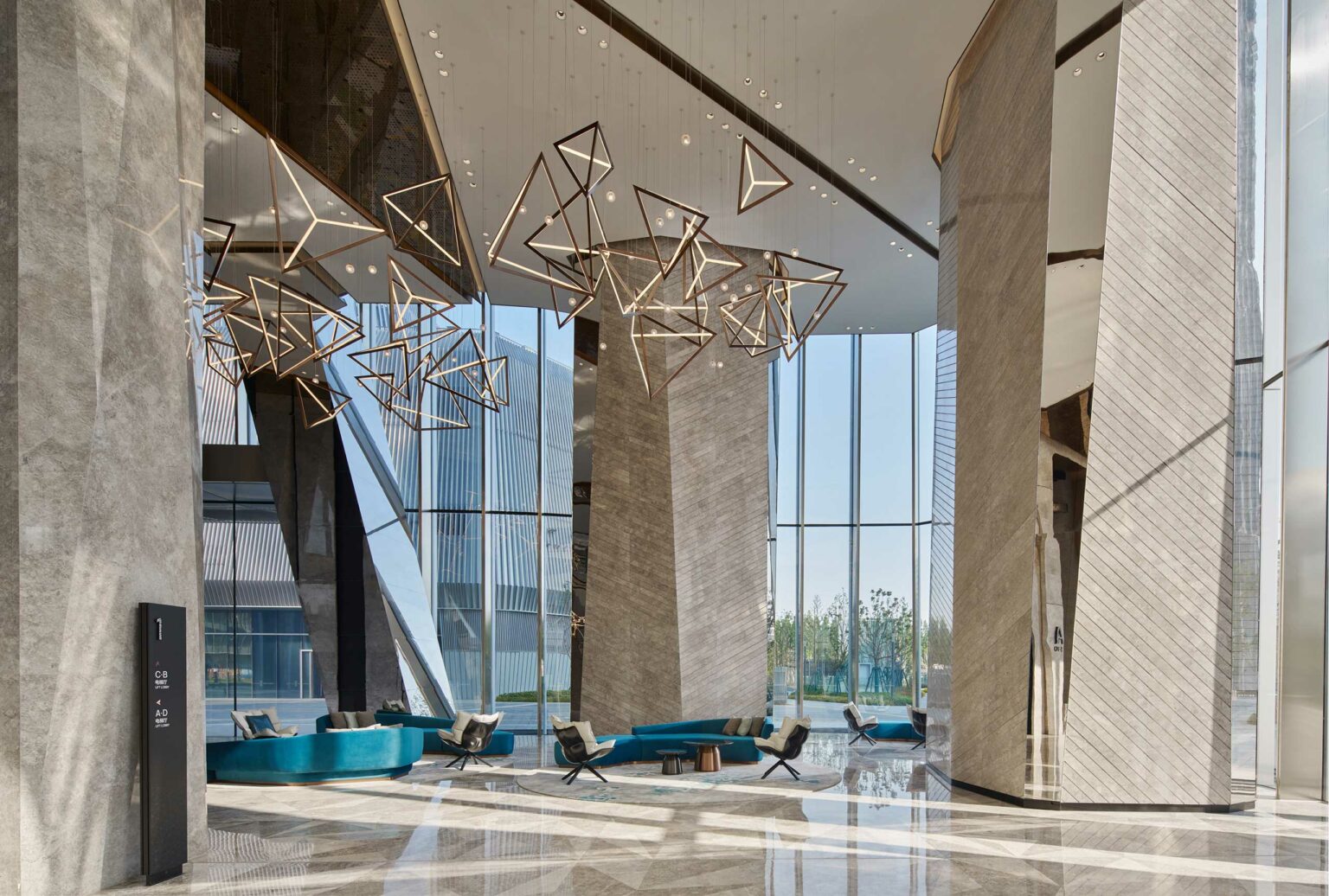 Modern office lobby with tall glass walls and geometric chandelier fixtures. Sleek teal seating and stone columns create an elegant, spacious atmosphere.
