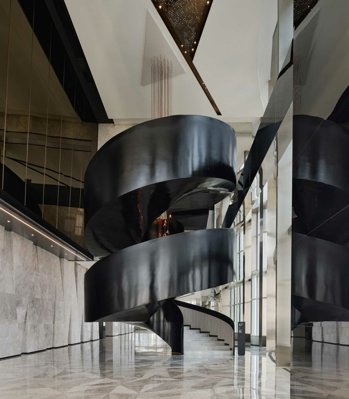 A sleek black spiral staircase in a modern commercial atrium, with glossy marble floors and large windows, creates an elegant, contemporary atmosphere.