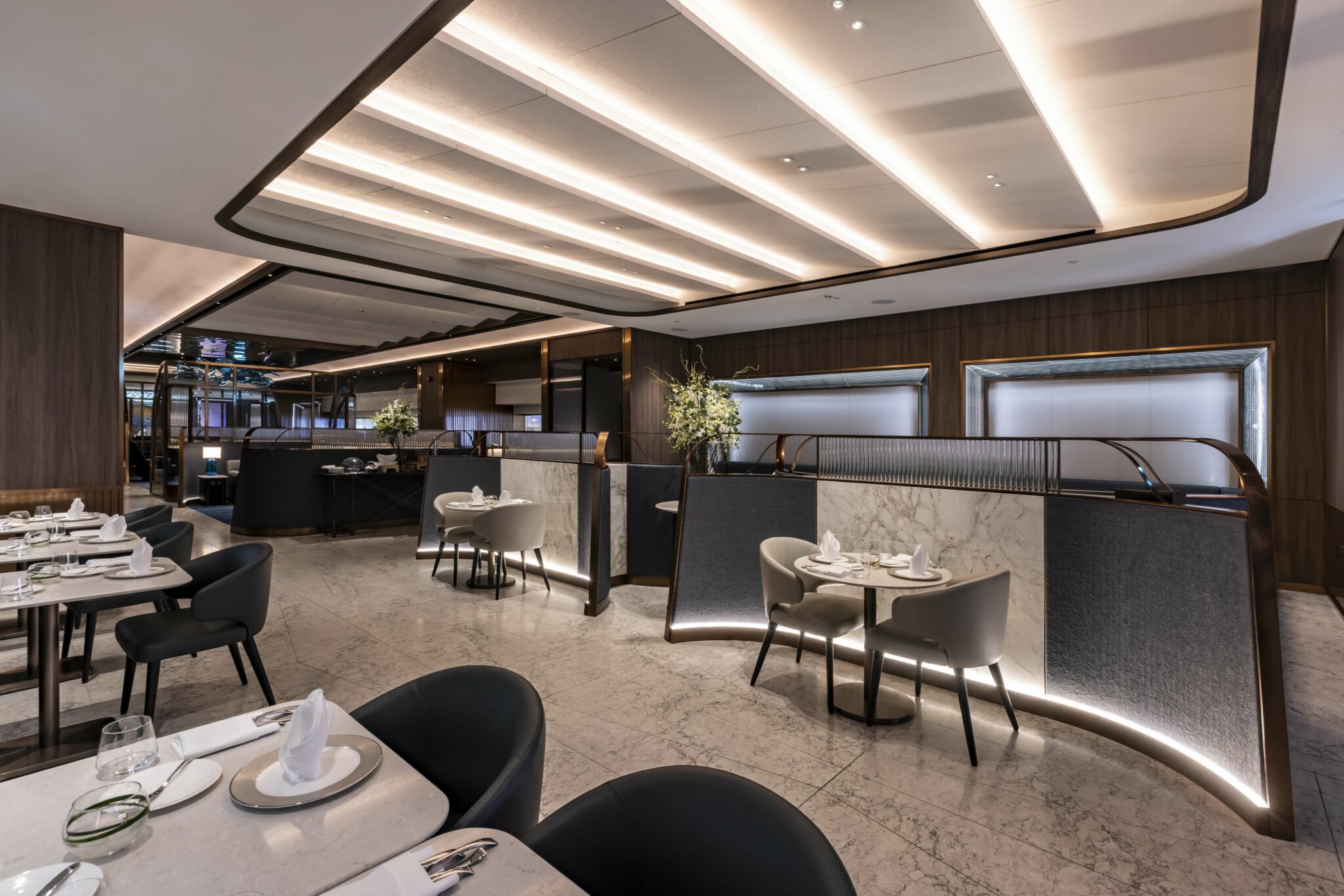 A sophisticated airline dining area with elegant tables set for guests, modern decor, and stylish partitions, creating a refined atmosphere perfect for enjoying a high-end culinary experience.