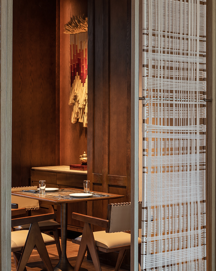 Cozy dining nook with wooden walls and a woven decoration. Features a small table set for two, soft lighting, and elegant, minimalist chairs.