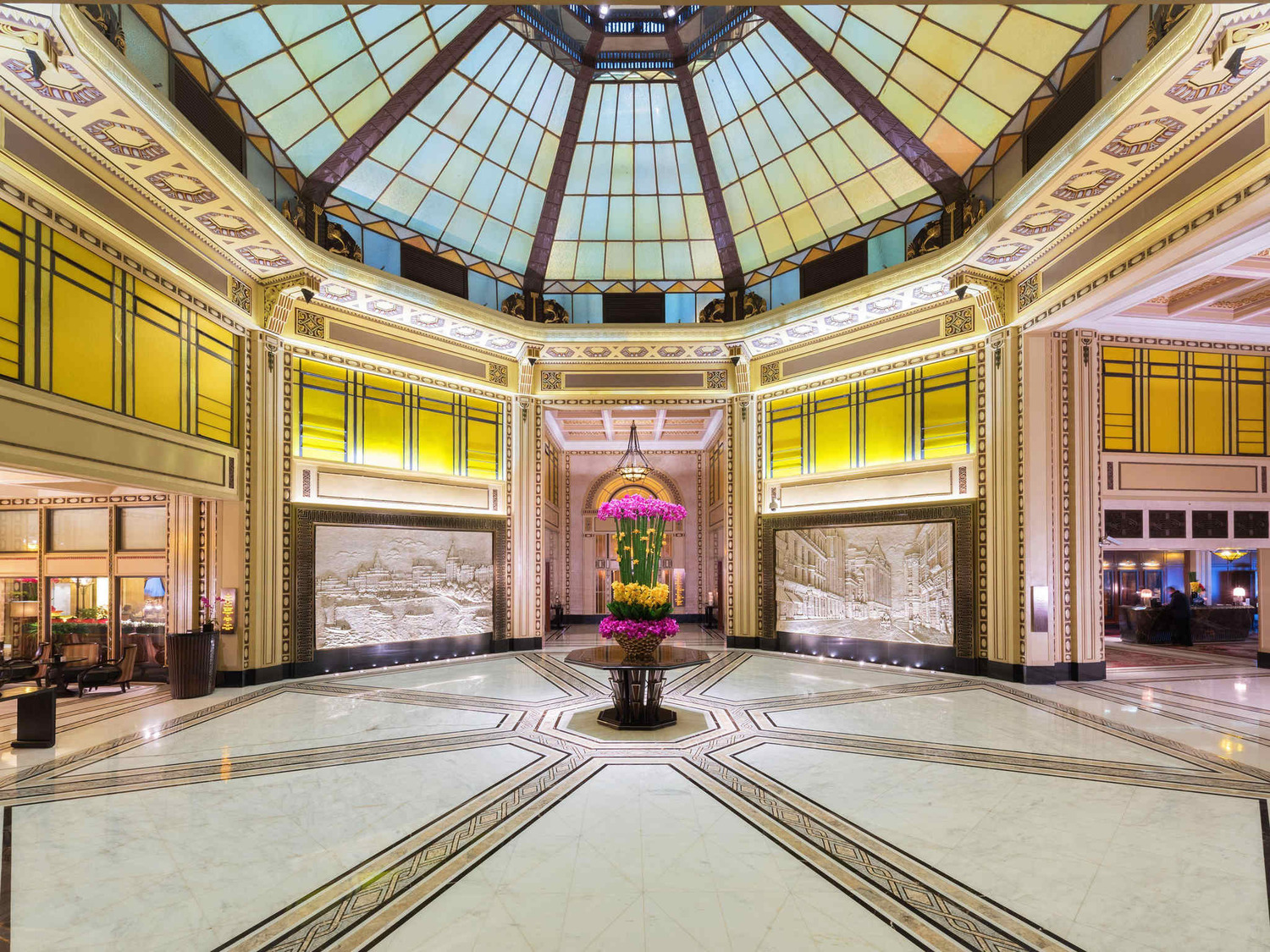 Luxurious hotel lobby adorned with a large, blooming pink cherry blossom tree. Elegant woman in traditional attire walks beneath a grand stained-glass dome.