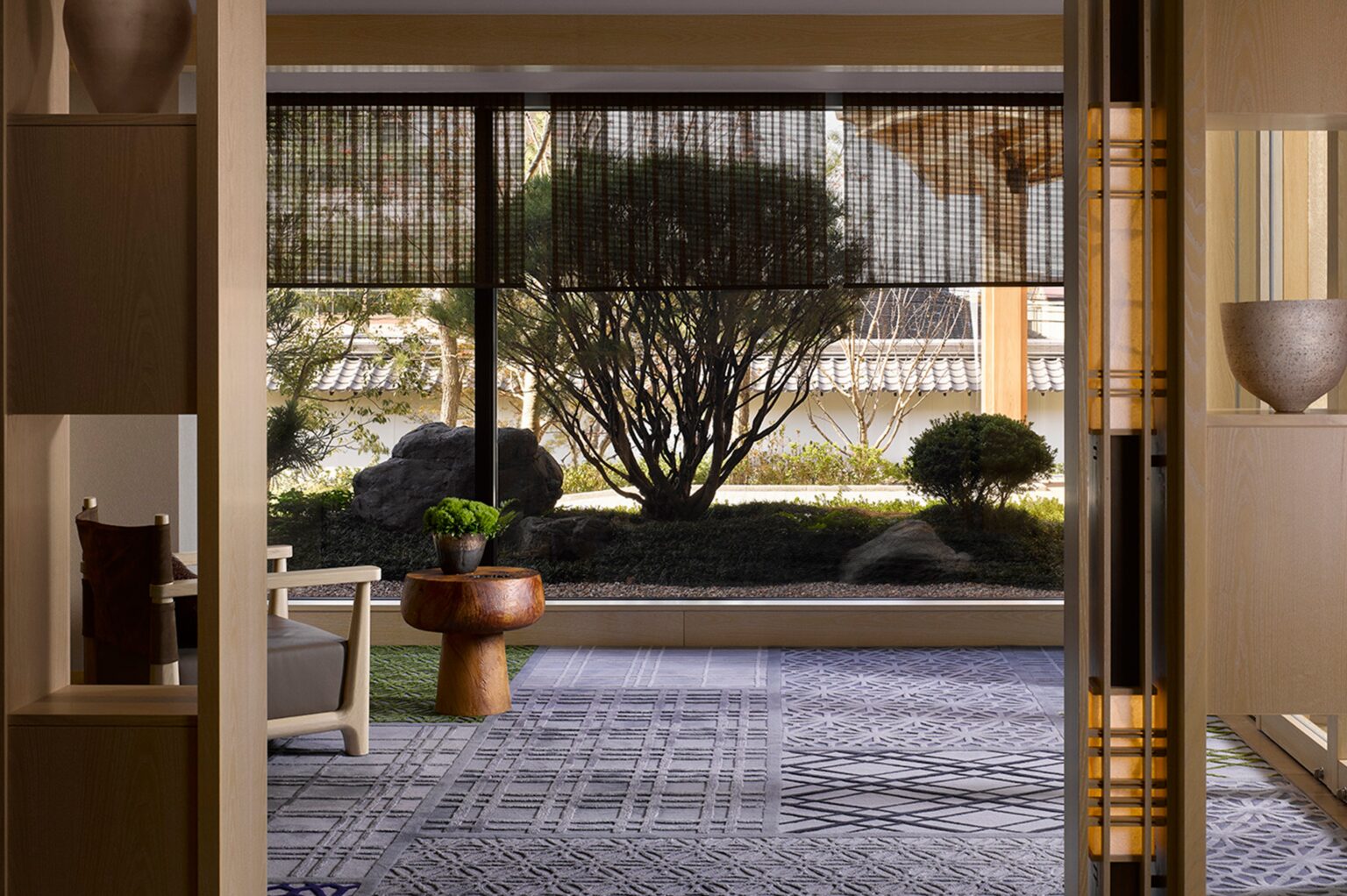 A tranquil interior view showcasing natural elements, with a cozy seating area, sliding screens, and a serene garden visible through large windows, creating a peaceful and harmonious atmosphere.
