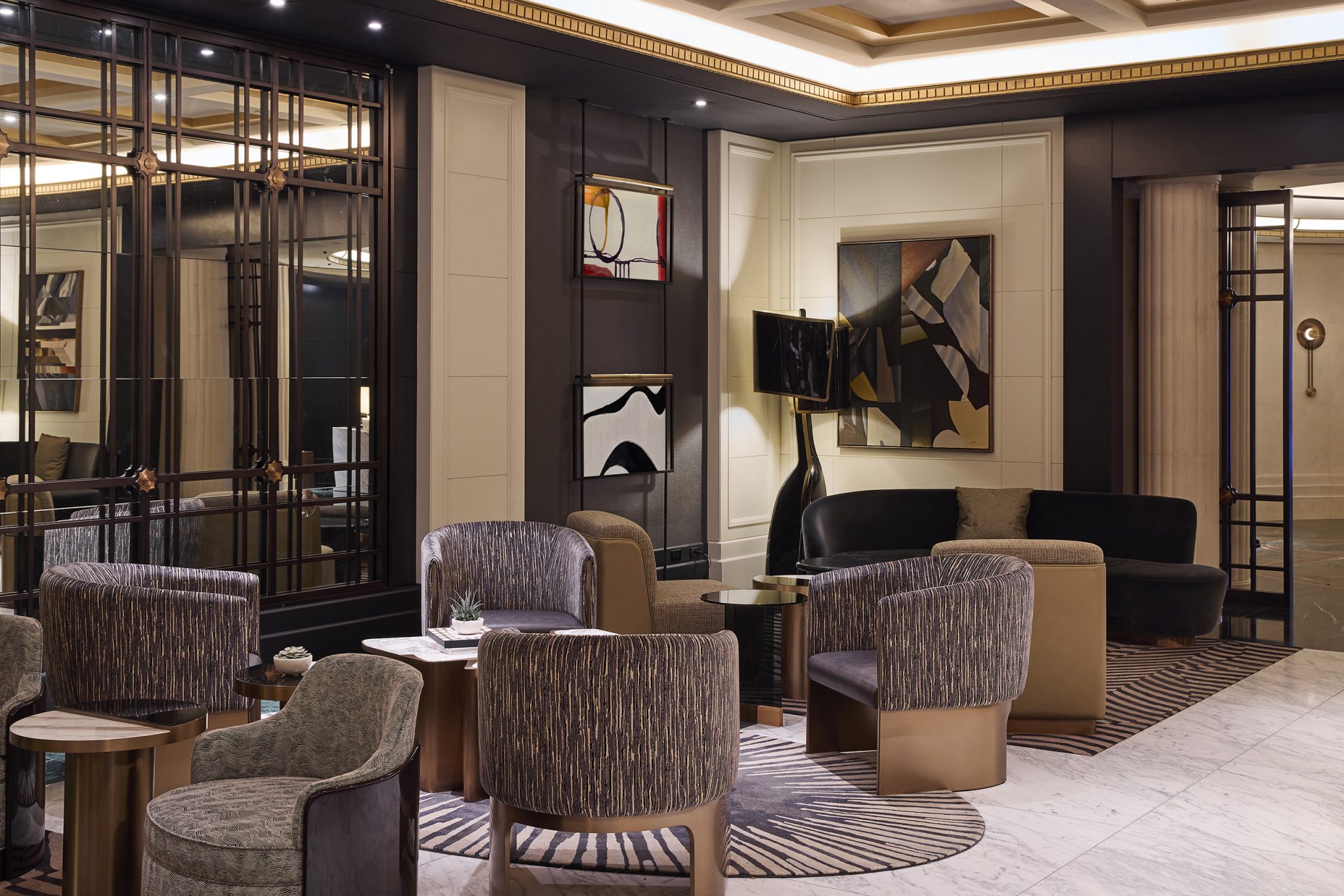 Elegant hotel lobby with modern decor. Features plush, patterned chairs, a black sofa, abstract art, soft lighting, and a sophisticated ambiance.