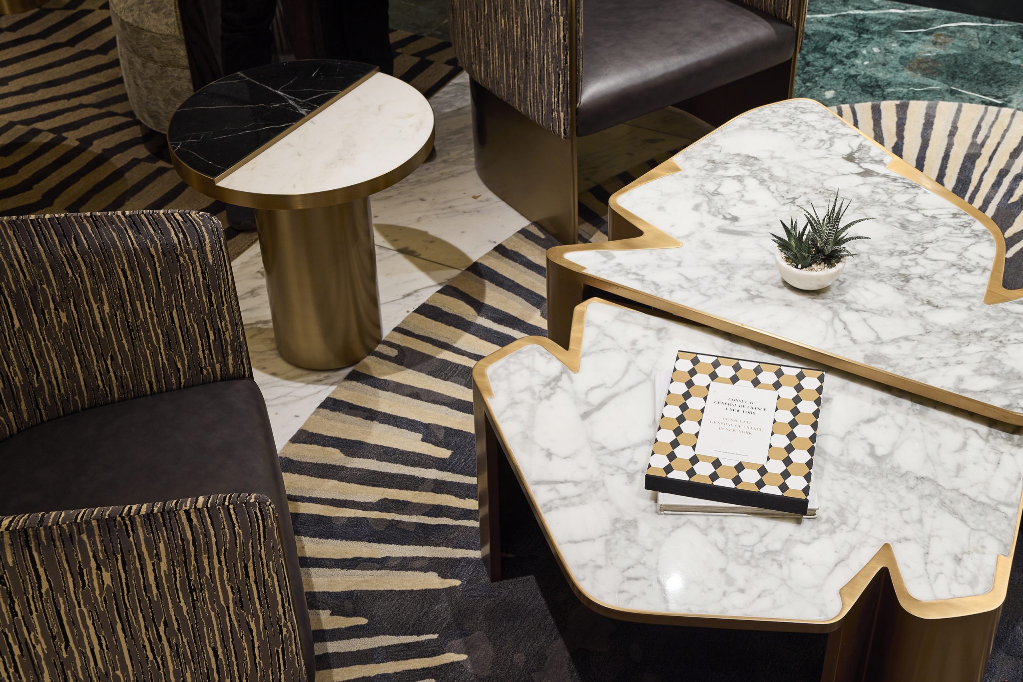 Luxuriously modern lounge with marble tables, geometric book, and a potted plant. Stylish chairs and zebra-patterned rug exude sophistication.
