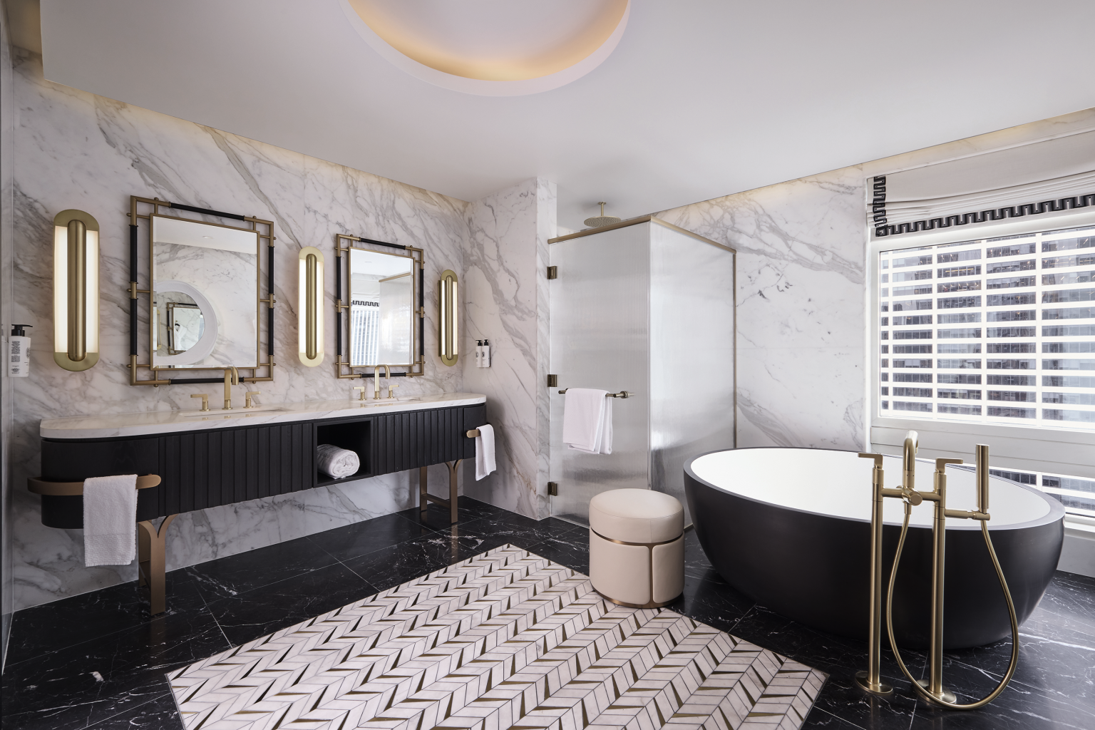 Luxurious bathroom with marble walls and black flooring. Features a black oval bathtub, dual sinks with mirrors, gold fixtures, and geometric rug.