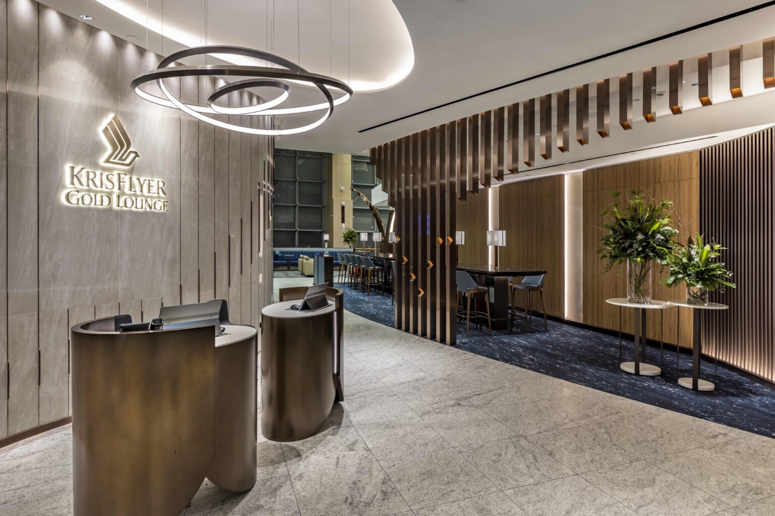 The modern entrance of the Singapore Airlines KrisFlyer Gold Lounge, featuring sleek reception desks, elegant lighting, and stylish decor, welcoming guests into a luxurious and comfortable space for relaxation.