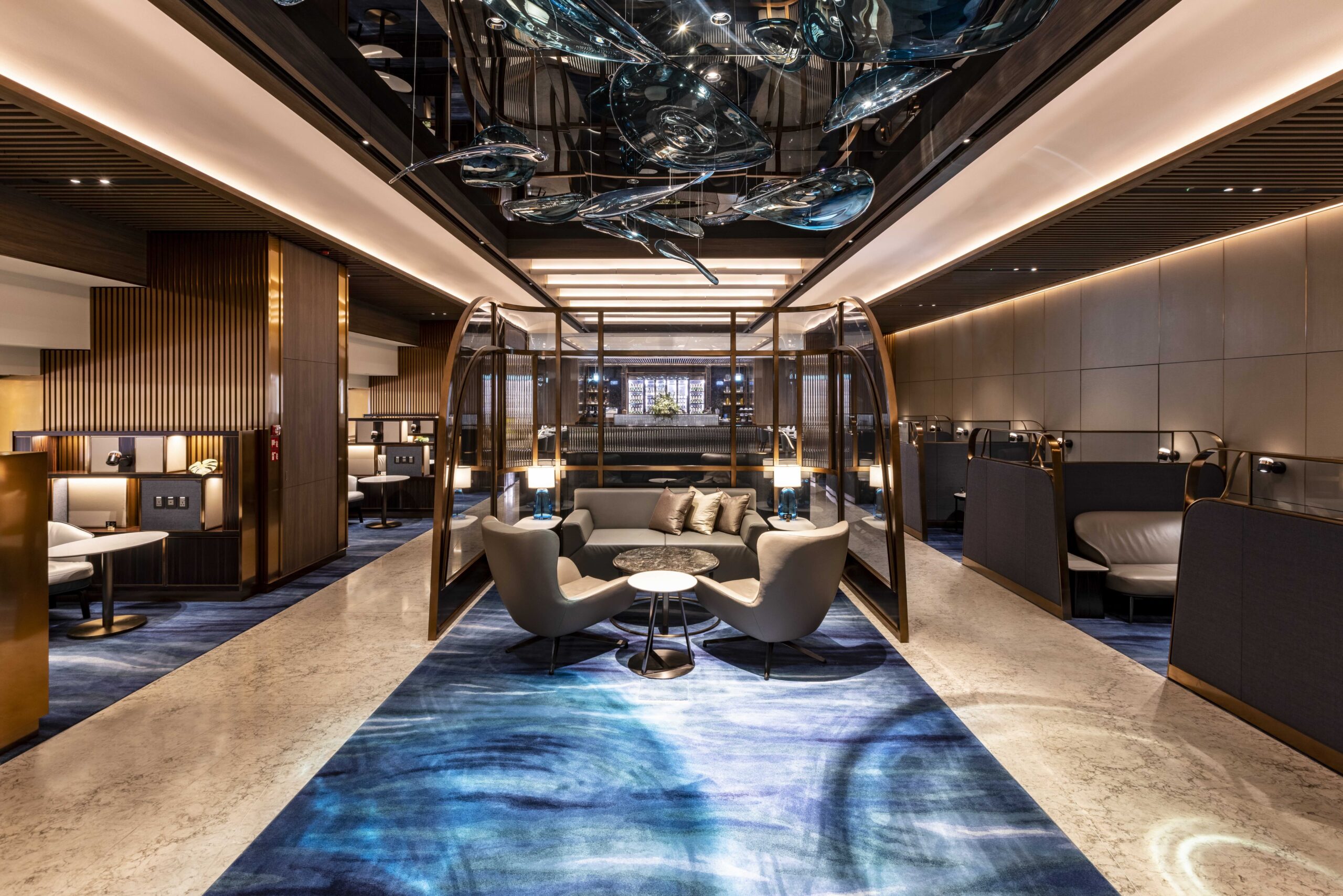 A cozy airline lounge area with modern seating, elegant decor, and artistic ceiling installations, creating an inviting and sophisticated atmosphere for relaxation.