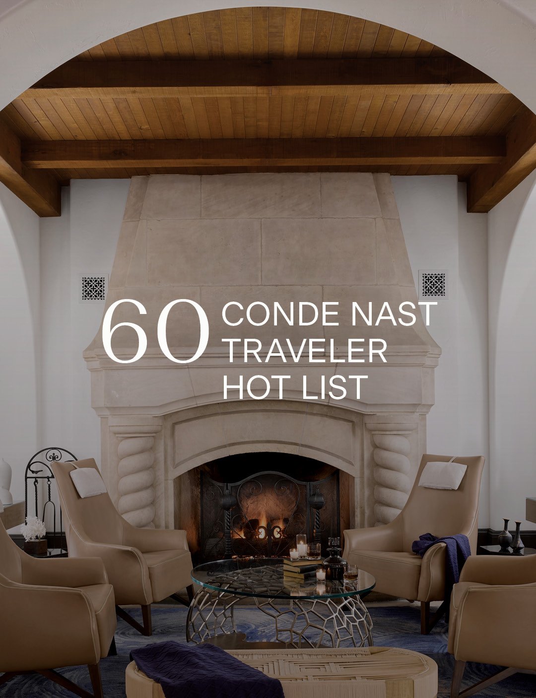 A cozy, elegant room with a large stone fireplace under a wooden beam ceiling. Two tan chairs and a round glass table create a warm, inviting atmosphere. Text reads 