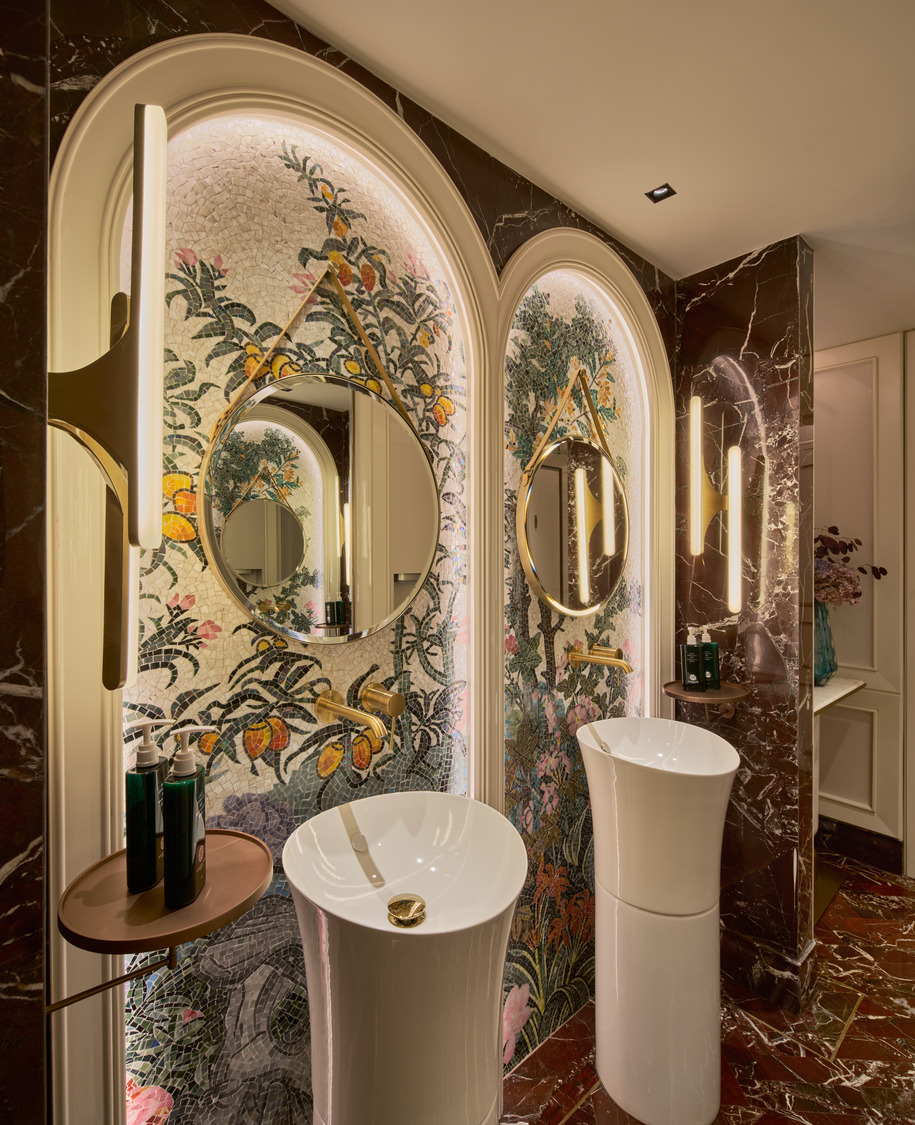 Artistic washroom with mosaic floral wall, round mirrors in arched niches, freestanding white sinks, and gold fixtures.