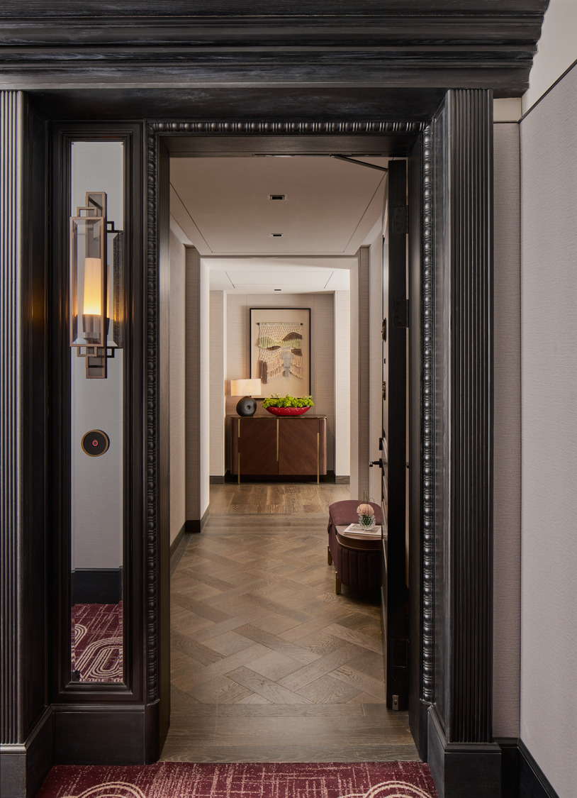 Elegant hallway with herringbone wood flooring, framed artwork, console table with red bowl, and decorative lighting.