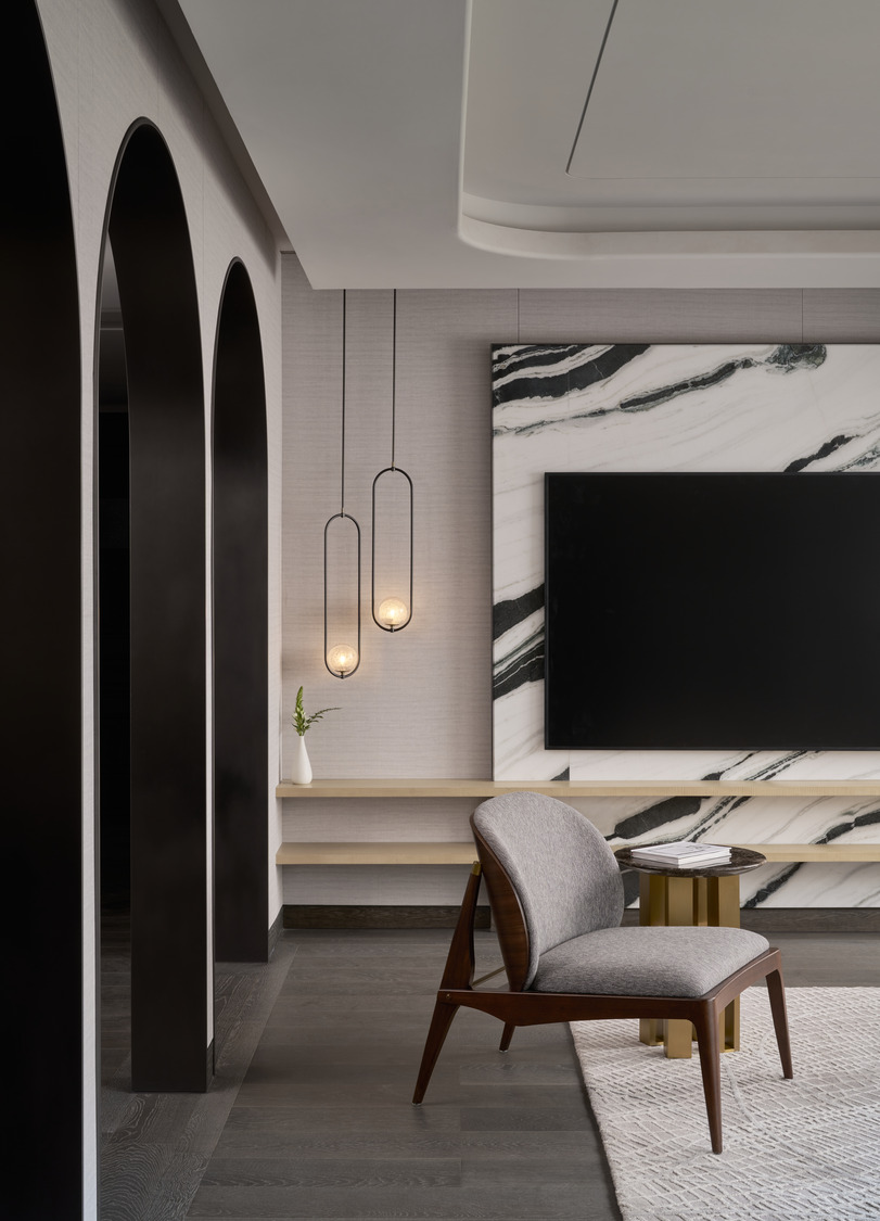 Modern lounge corner with grey upholstered chair, marble feature wall, floating shelves, and pendant lights framed by dark arched openings.