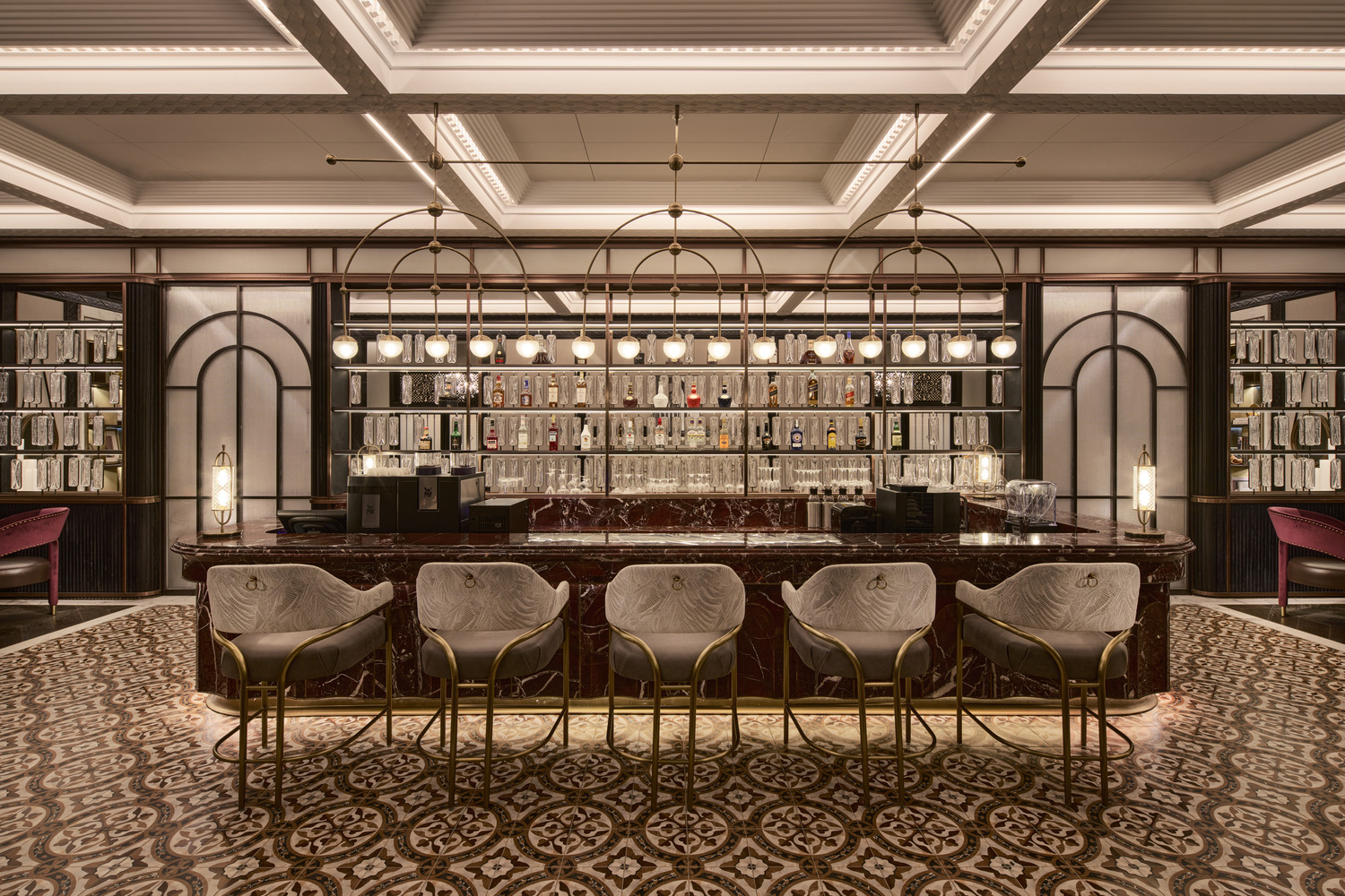 Opulent bar with marble counter, patterned tile flooring, arched shelving, and pendant lighting creating a refined atmosphere.