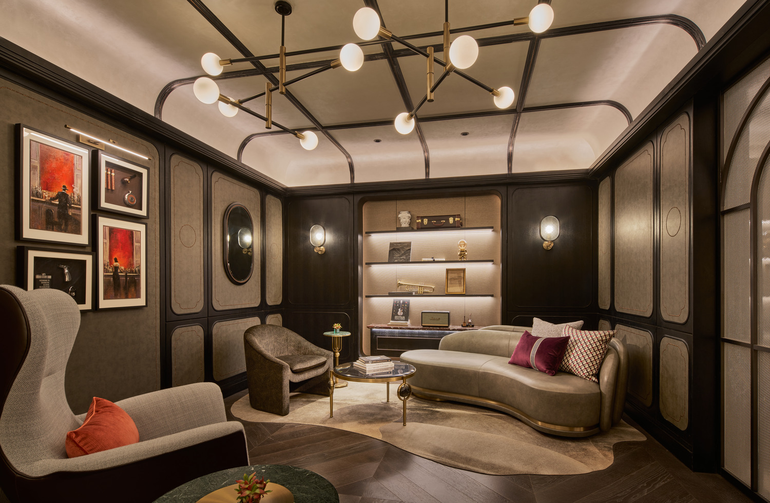 Sophisticated lounge with sculptural sofa, accent chairs, wall art, and illuminated shelving displaying books and collectibles.