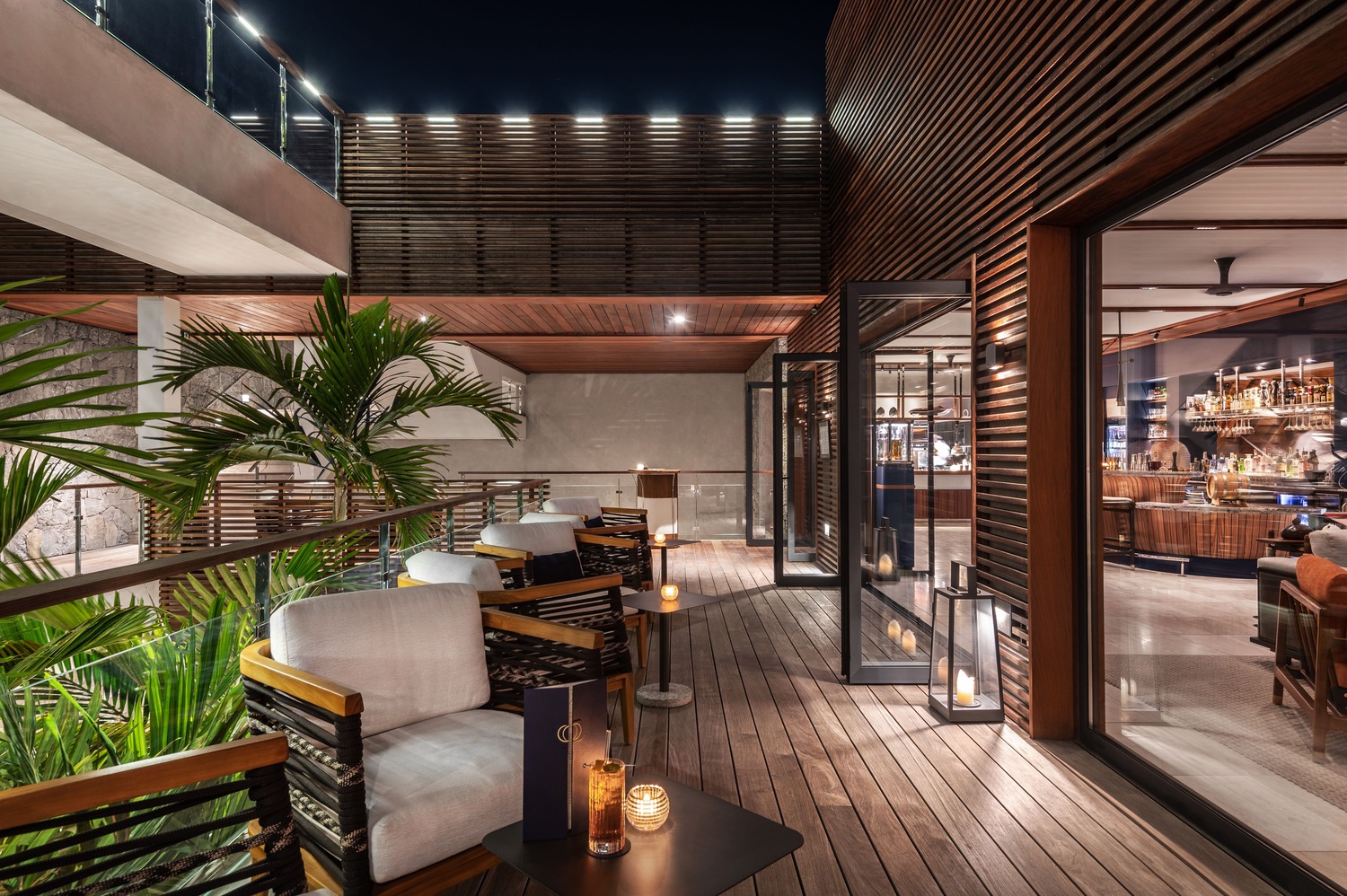 Outdoor terrace with lounge seating, palm trees, and candlelit tables overlooking the bar area at Ocean Club St Barths.
