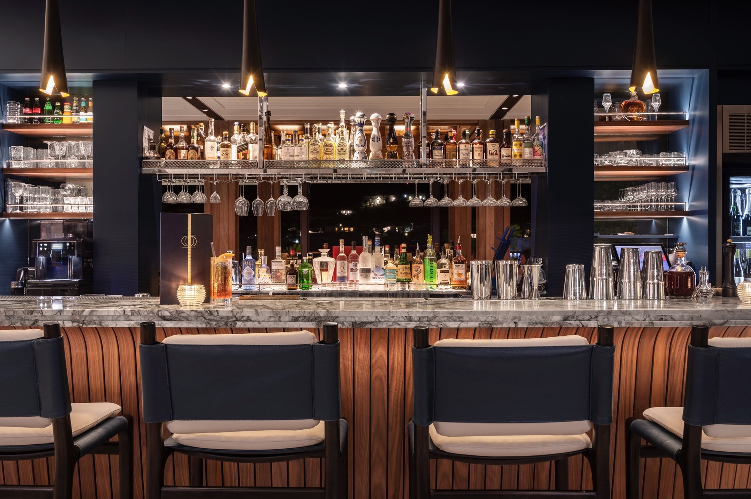 Elegant marble-topped bar with backlit shelving and suspended glass racks at Ocean Club St Barths.