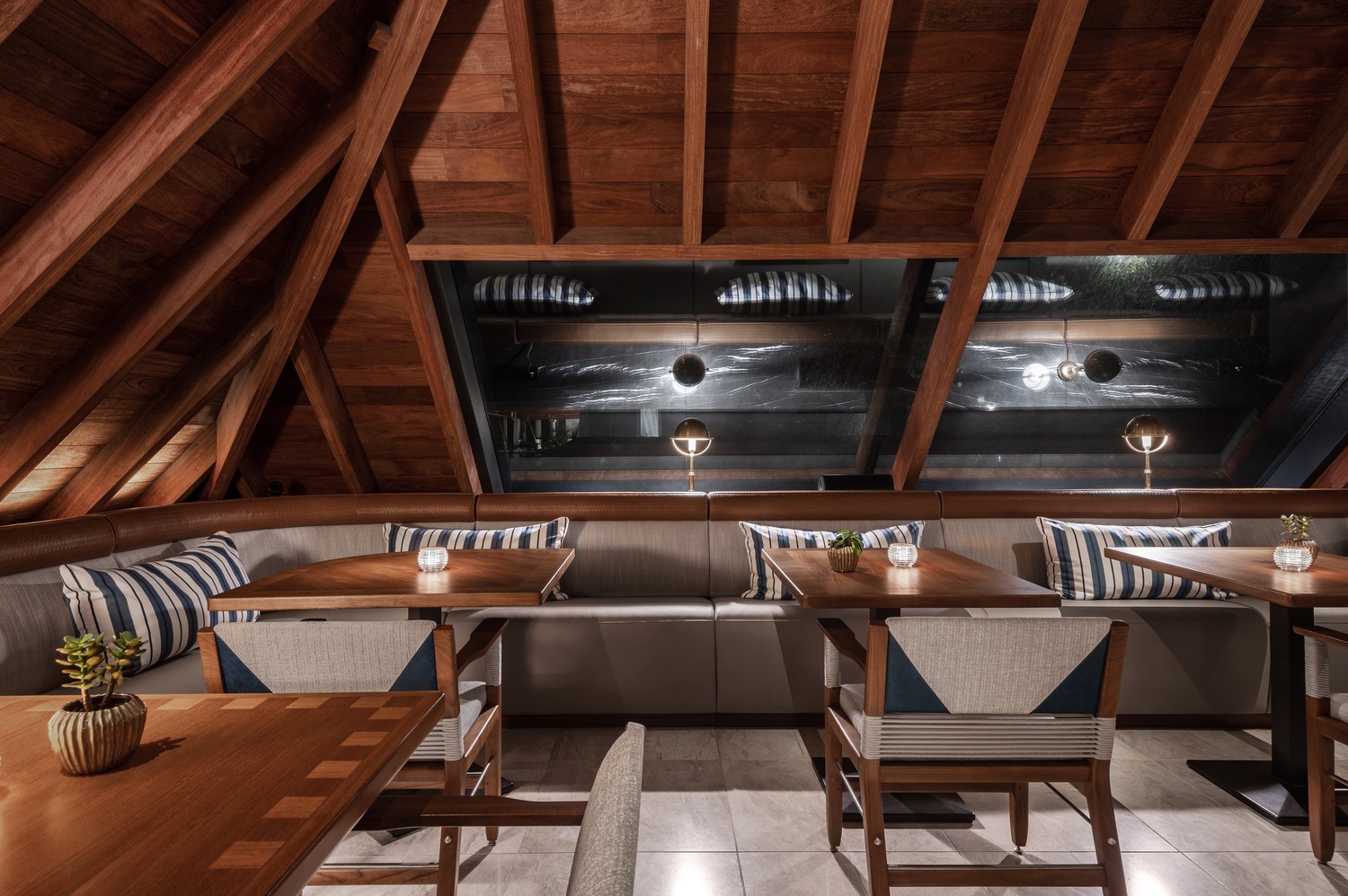 Intimate dining alcove with angled wooden ceiling, striped cushions, and warm ambient lighting at Ocean Club St Barths.