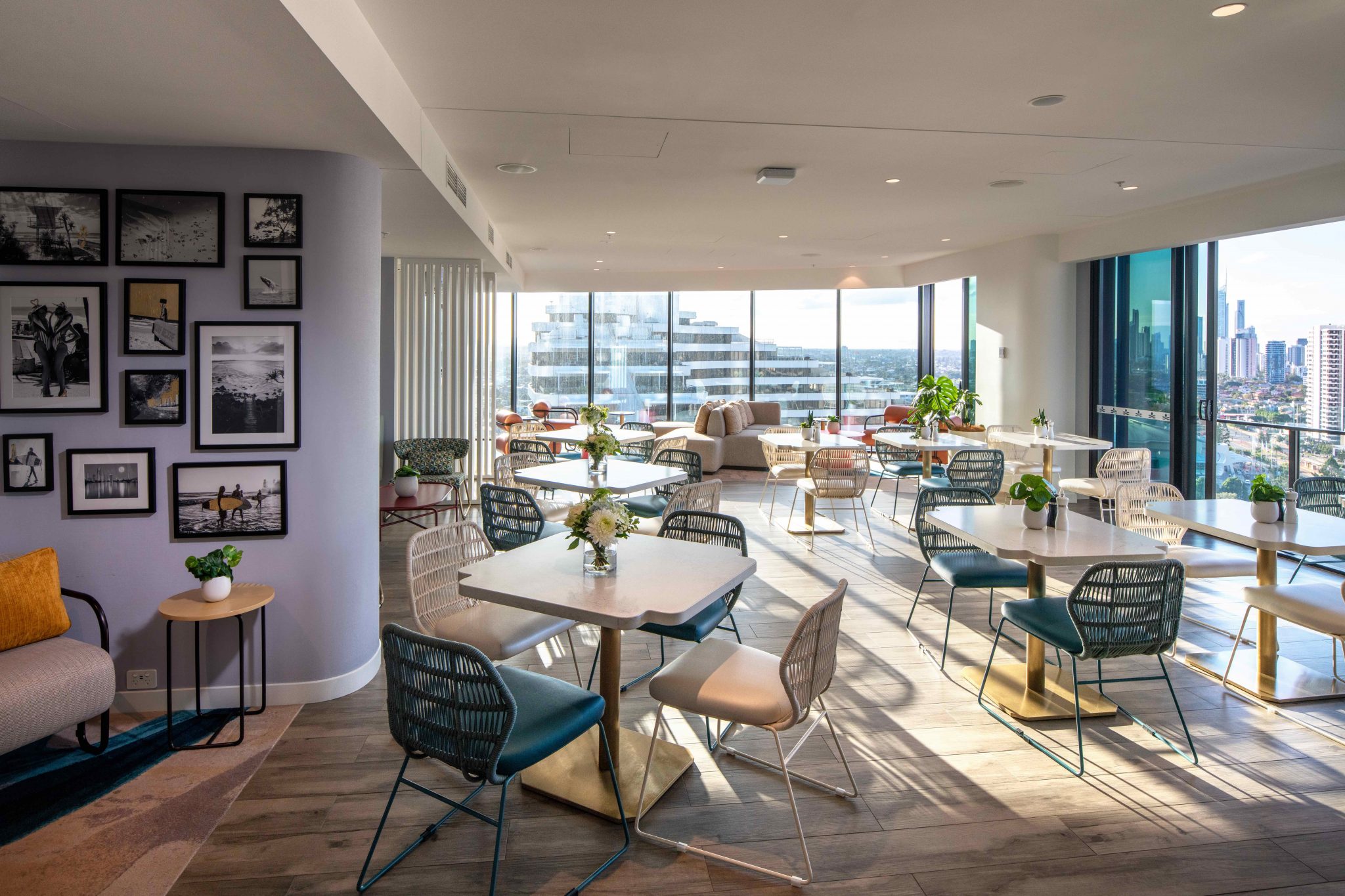 Modern hotel restaurant with elegant decor, featuring turquoise and beige chairs, wooden tables, and striking overhead lights, creating a sophisticated ambiance.