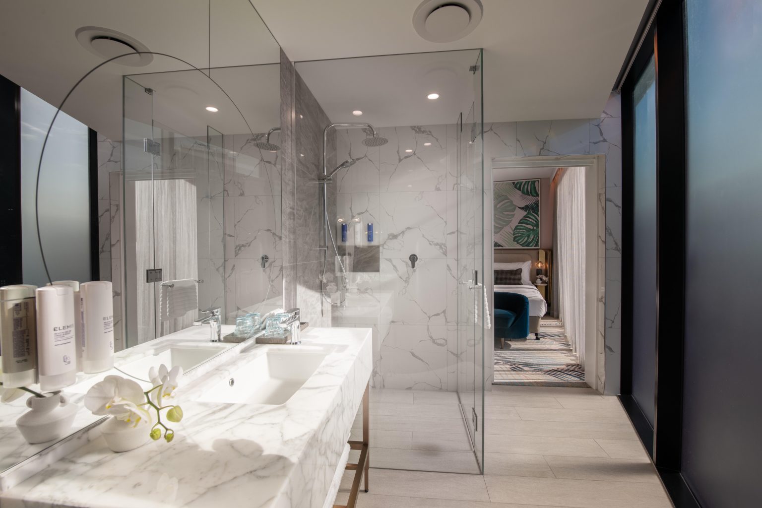 Luxurious hotel suite with modern decor, featuring a plush bed, abstract art, a large TV, and elegant seating. Warm lighting creates a cozy ambiance.