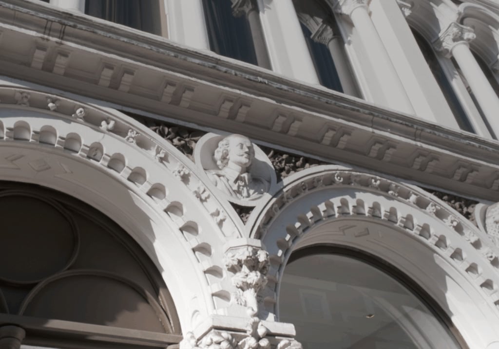 HBA London studio's exterior. Ornate architectural detail showing a sculpted man's bust in a roundel, framed by decorative arches and floral motifs on a historic building façade.