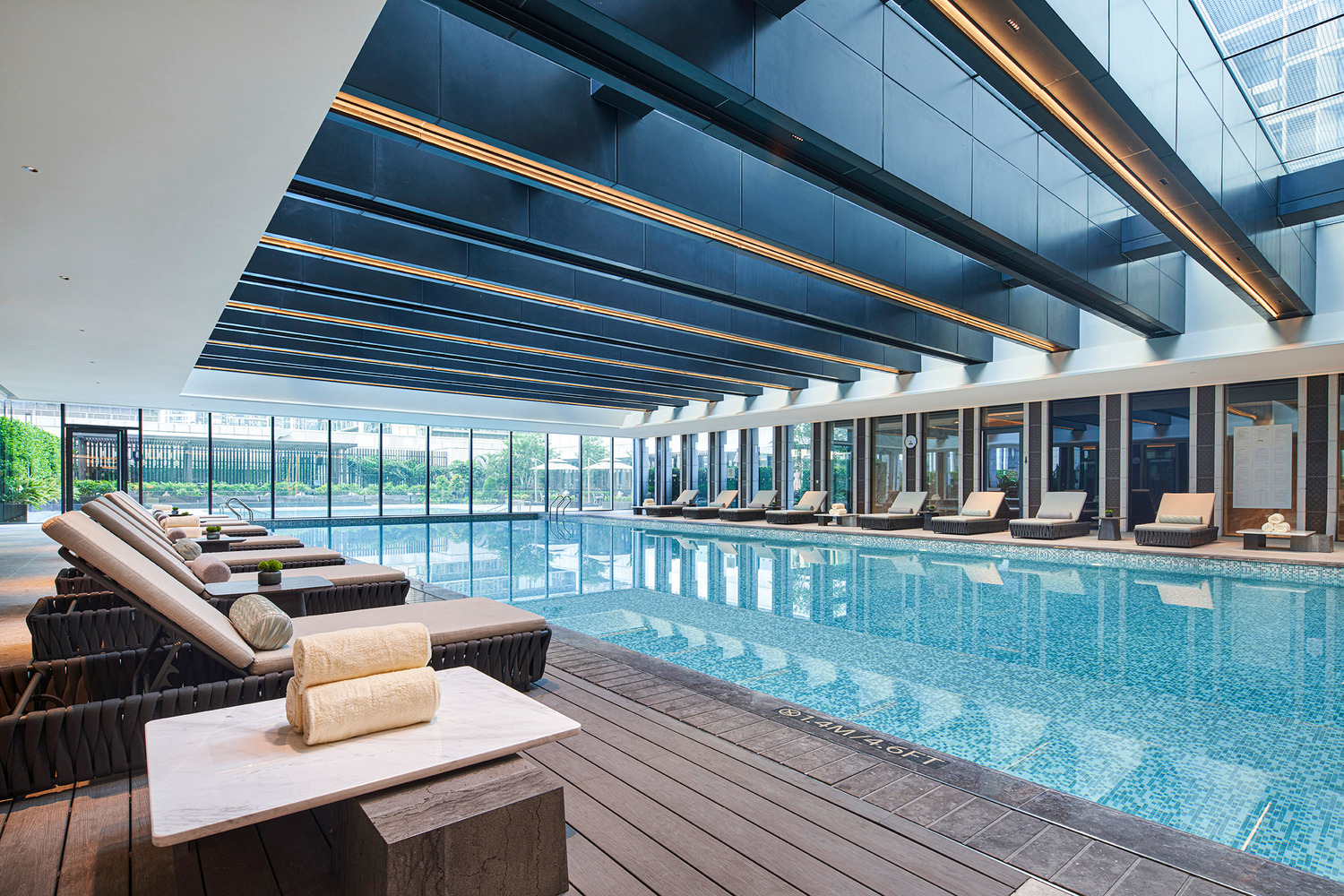 Indoor pool area with large skylight, surrounded by potted plants and modern sun loungers. The space feels serene, with trees visible outside.