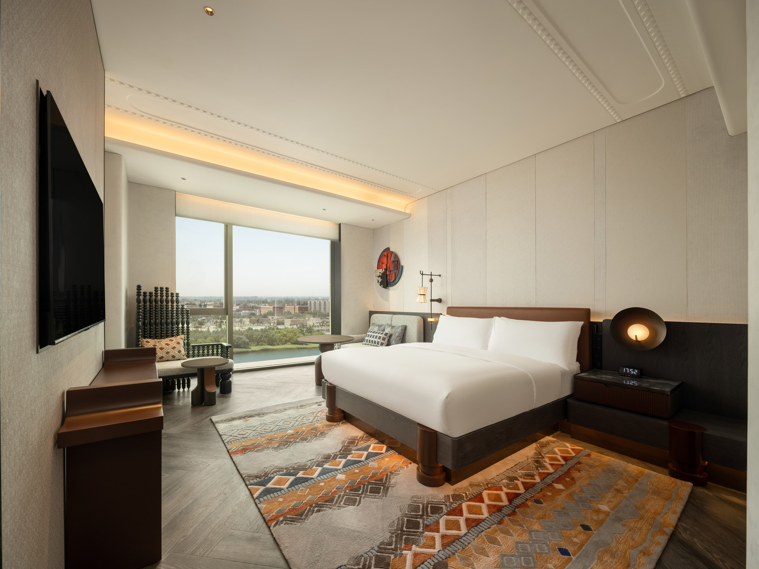 Luxurious hotel suite with modern decor, featuring a plush bed, abstract art, a large TV, and elegant seating. Warm lighting creates a cozy ambiance.