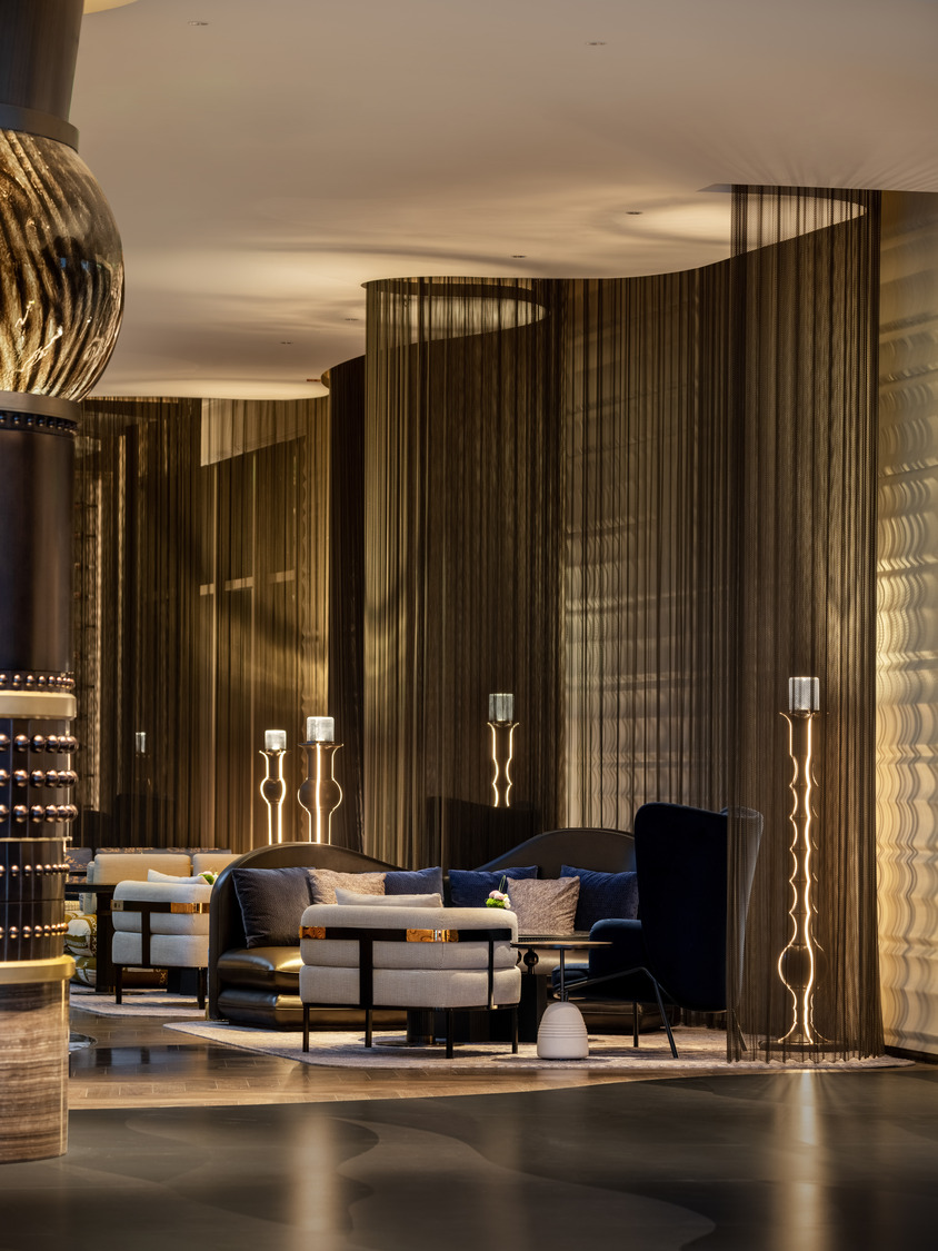 A grand hotel lobby featuring a dramatic chandelier, elegant seating areas, and a sweeping staircase, creating a luxurious and inviting atmosphere for guests to relax and socialize.