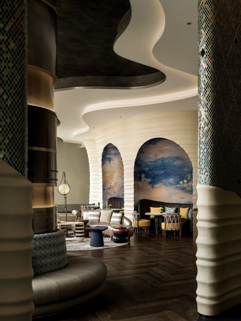 A grand hotel lobby featuring a dramatic chandelier, elegant seating areas, and a sweeping staircase, creating a luxurious and inviting atmosphere for guests to relax and socialize.