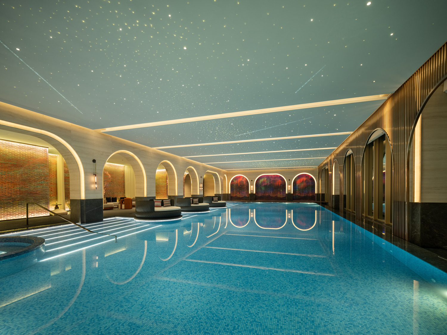 Indoor pool area with large skylight, surrounded by potted plants and modern sun loungers. The space feels serene, with trees visible outside.
