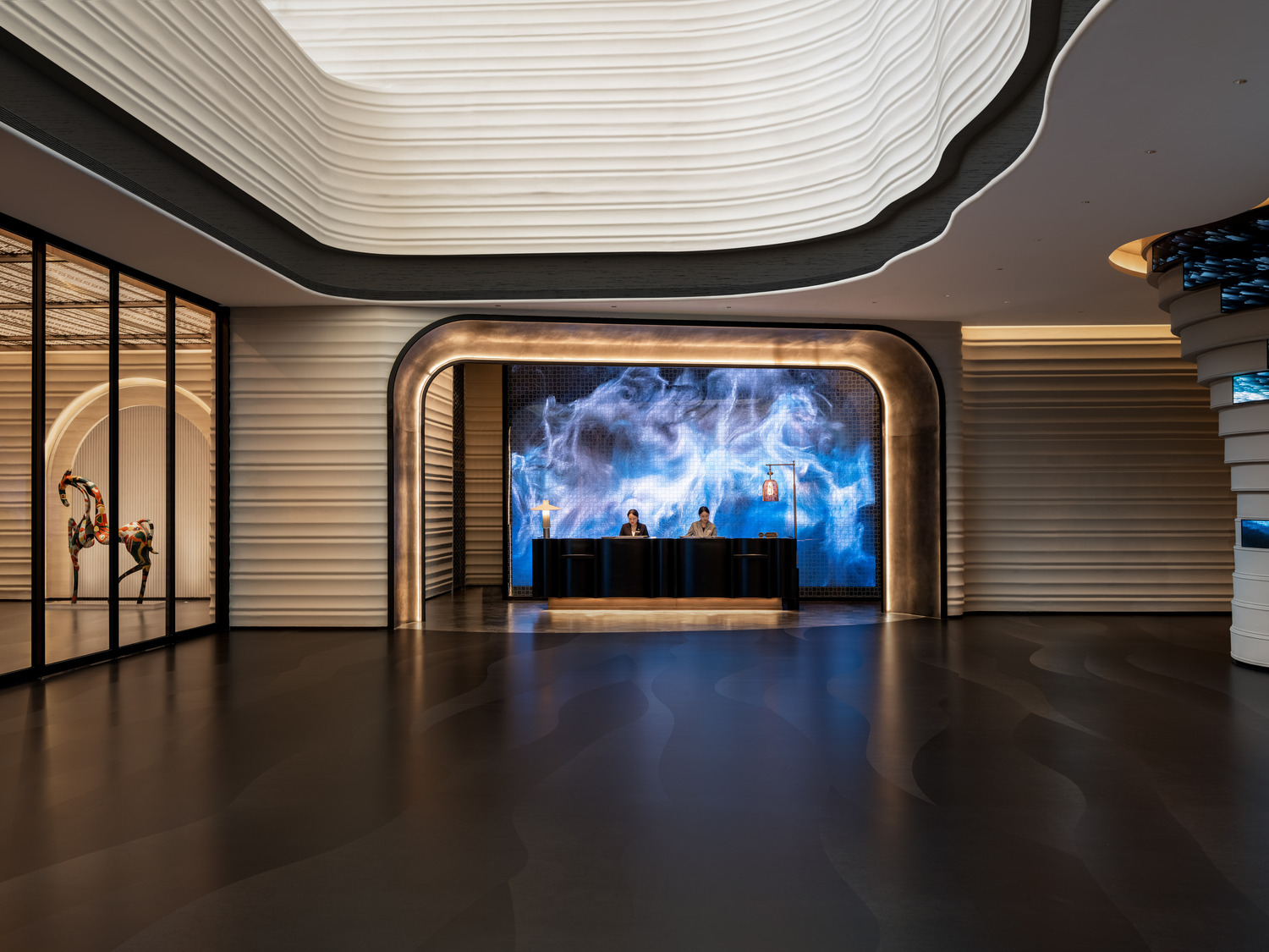A grand hotel lobby featuring a dramatic chandelier, elegant seating areas, and a sweeping staircase, creating a luxurious and inviting atmosphere for guests to relax and socialize.
