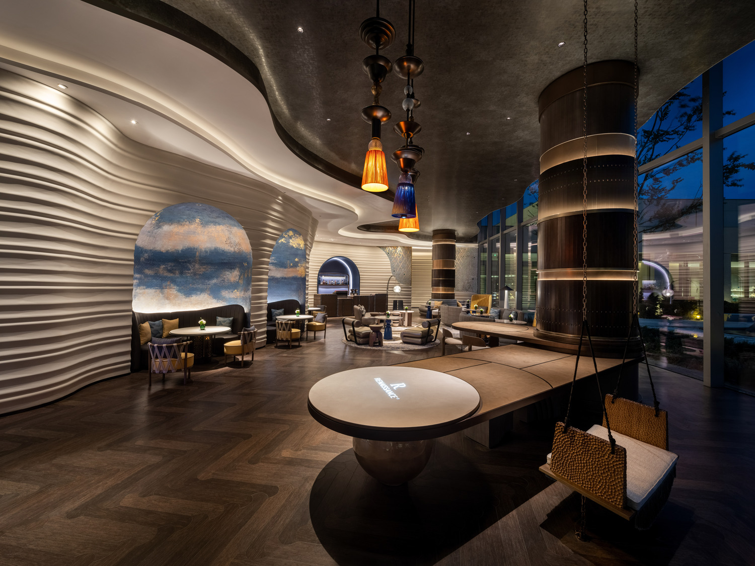 A grand hotel lobby featuring a dramatic chandelier, elegant seating areas, and a sweeping staircase, creating a luxurious and inviting atmosphere for guests to relax and socialize.