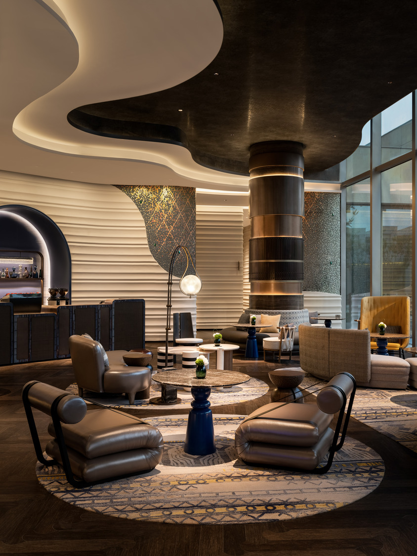 A grand hotel lobby featuring a dramatic chandelier, elegant seating areas, and a sweeping staircase, creating a luxurious and inviting atmosphere for guests to relax and socialize.