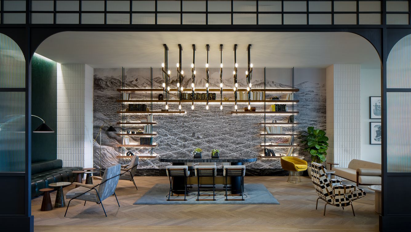 elegant hotel lounge with dim lighting, featuring round tables, plush chairs, and a sleek bar in the background. The ambiance is cozy and sophisticated.