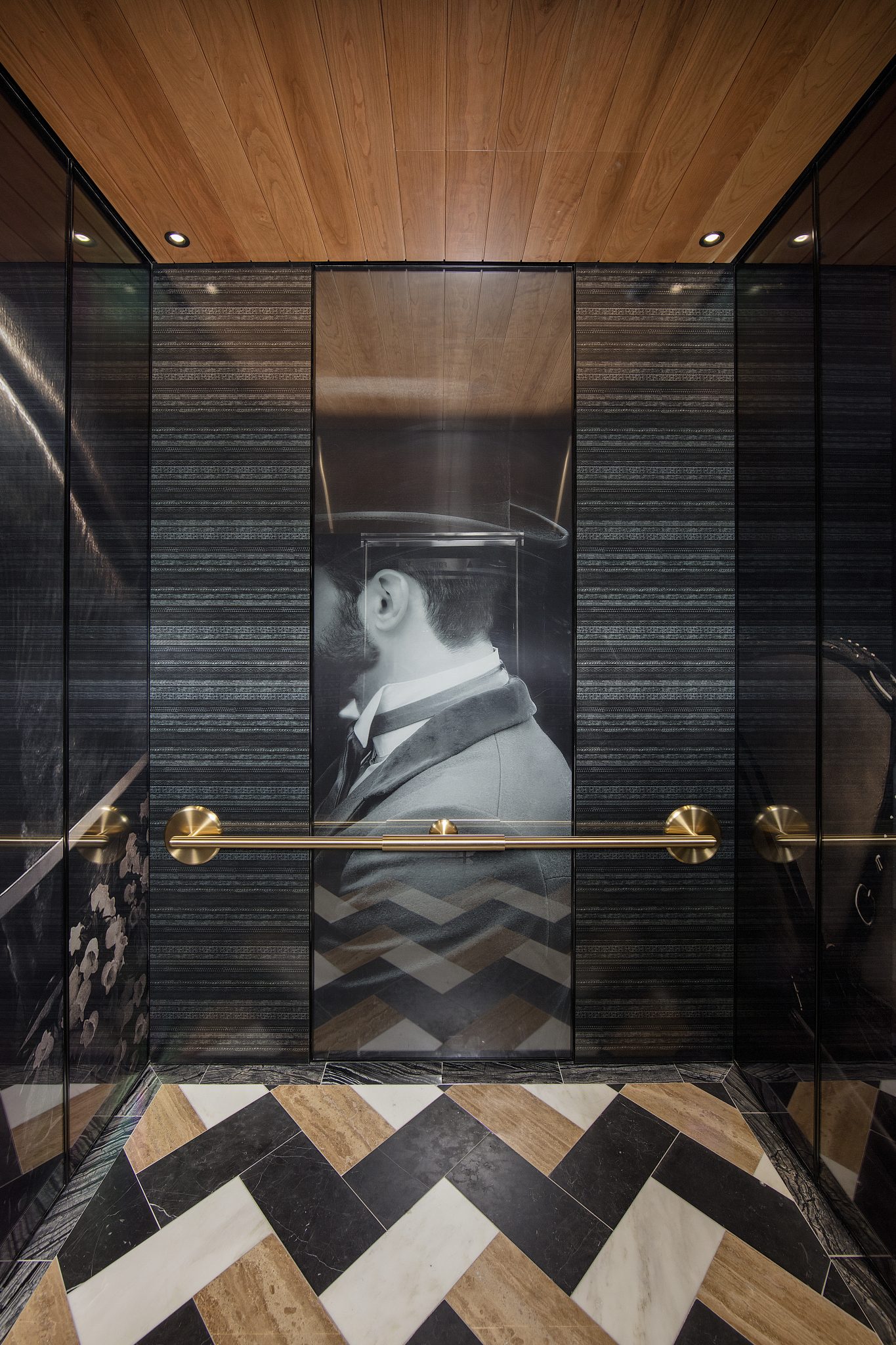 Luxurious modern hotel elevator interior with beige marble walls and geometric panels. Central art piece features metallic blue circles, creating elegance.