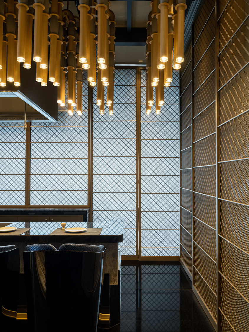 Elegant modern restaurant interior within a luxurious resort featuring geometric ceiling lights, wooden floors, and stylish beige chairs around round tables, creating a warm, inviting ambiance.