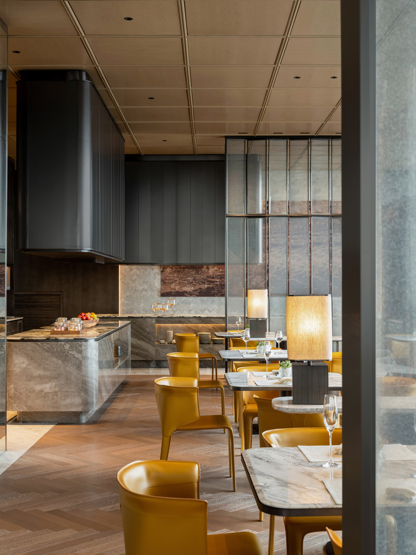 Elegant modern restaurant interior within a luxurious resort featuring geometric ceiling lights, wooden floors, and stylish beige chairs around round tables, creating a warm, inviting ambiance.