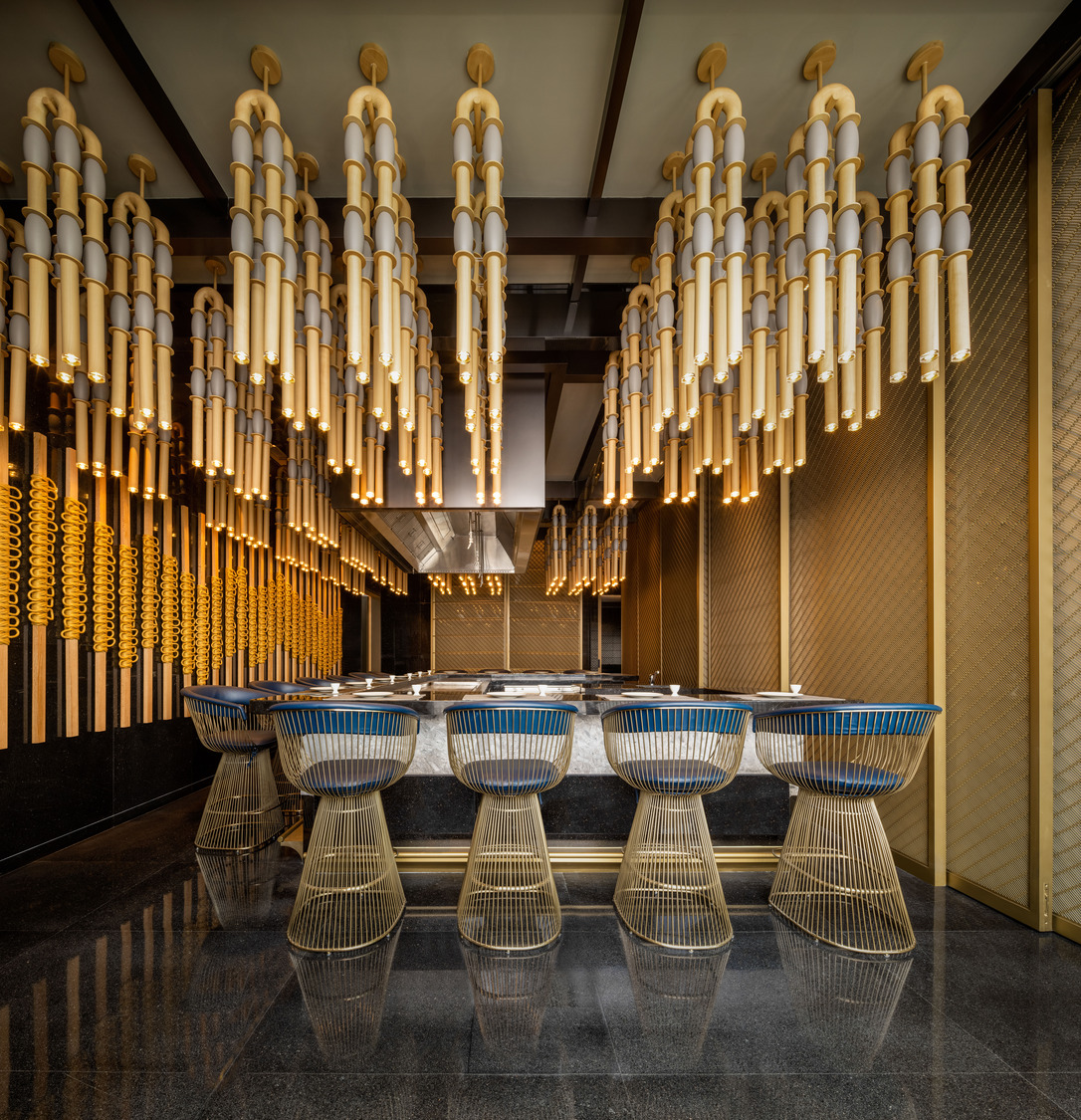 Elegant modern restaurant interior within a luxurious resort featuring geometric ceiling lights, wooden floors, and stylish beige chairs around round tables, creating a warm, inviting ambiance.