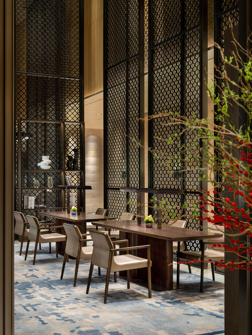 Modern hotel lobby with a sleek marble reception desk, vibrant teal and red shelving, elegant lighting, and a lush indoor tree. The space conveys luxury.