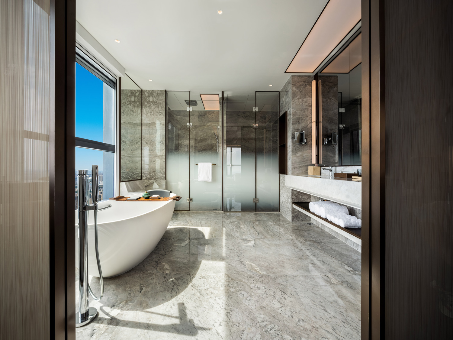 Modern bathroom with a freestanding oval tub, beige tile walls, a large window with sheer curtains, minimalist decor, and a serene, luxurious ambiance.