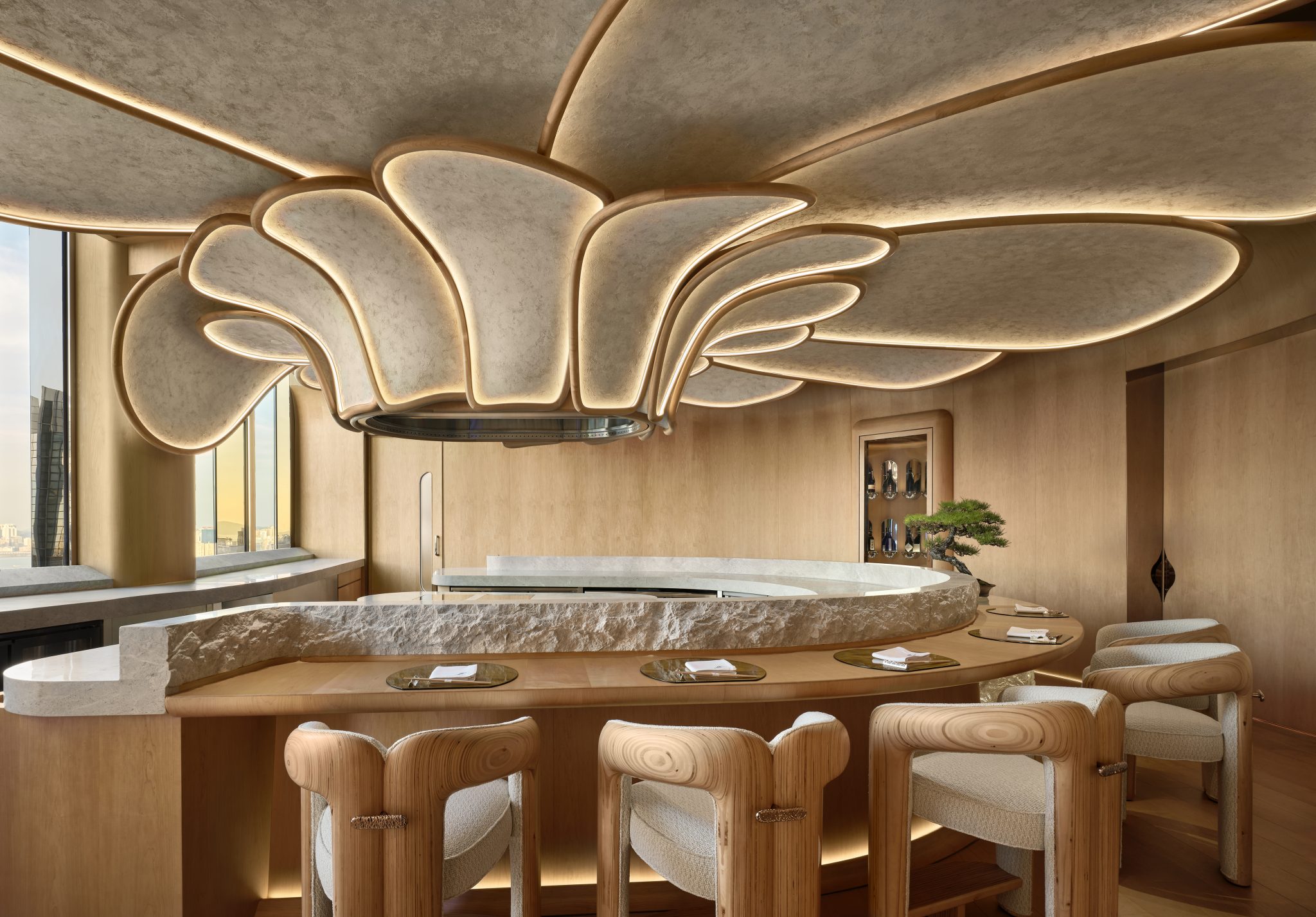 2. Elegant interior of a modern bar with a sculptural, petal-like ceiling. Curved stone counter, plush wooden chairs, and a small bonsai add sophistication.