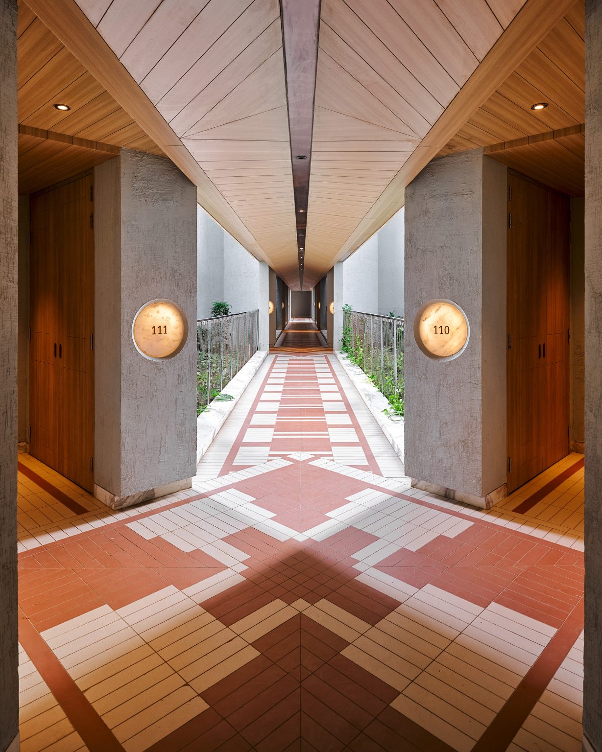 A modern hotel corridor with warm, wooden accents and patterned flooring. Rooms 110 and 111 are visible, creating a sense of symmetry and calm.