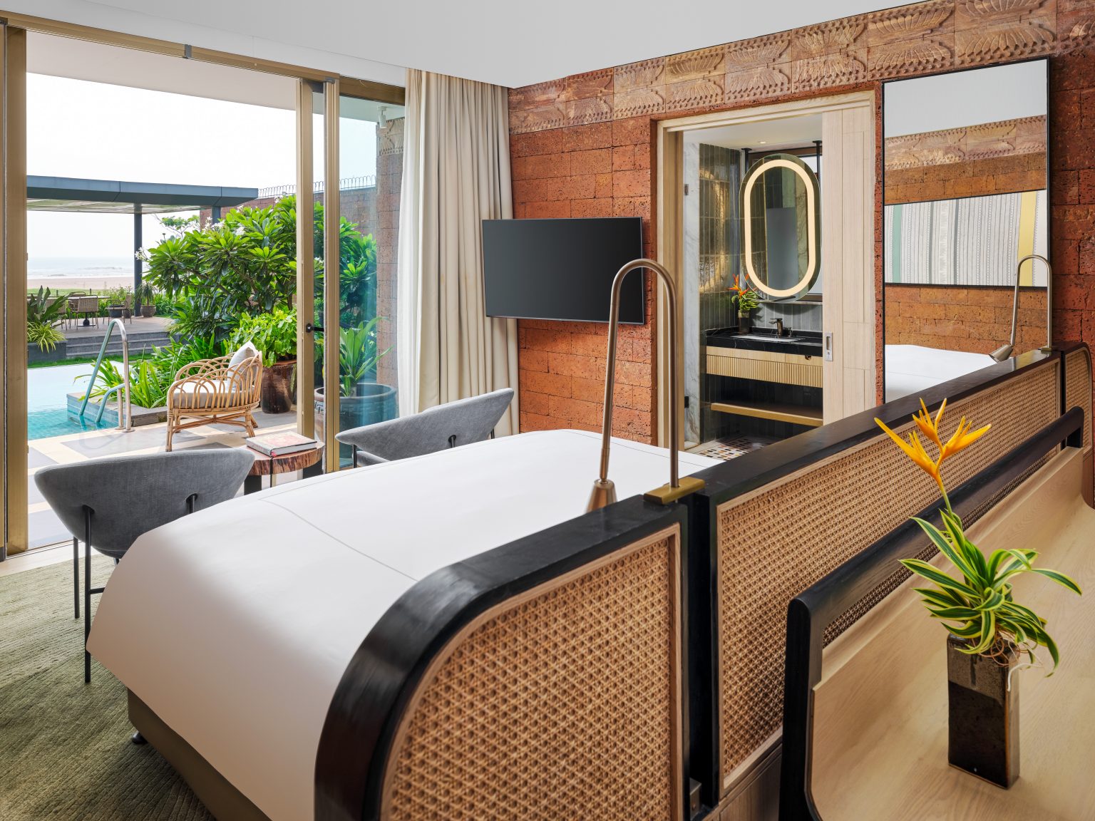 Luxurious hotel room with a pool view. Features a stylish bed, warm lighting, plants, wicker chairs, and a modern bathroom. Calm and inviting ambiance.