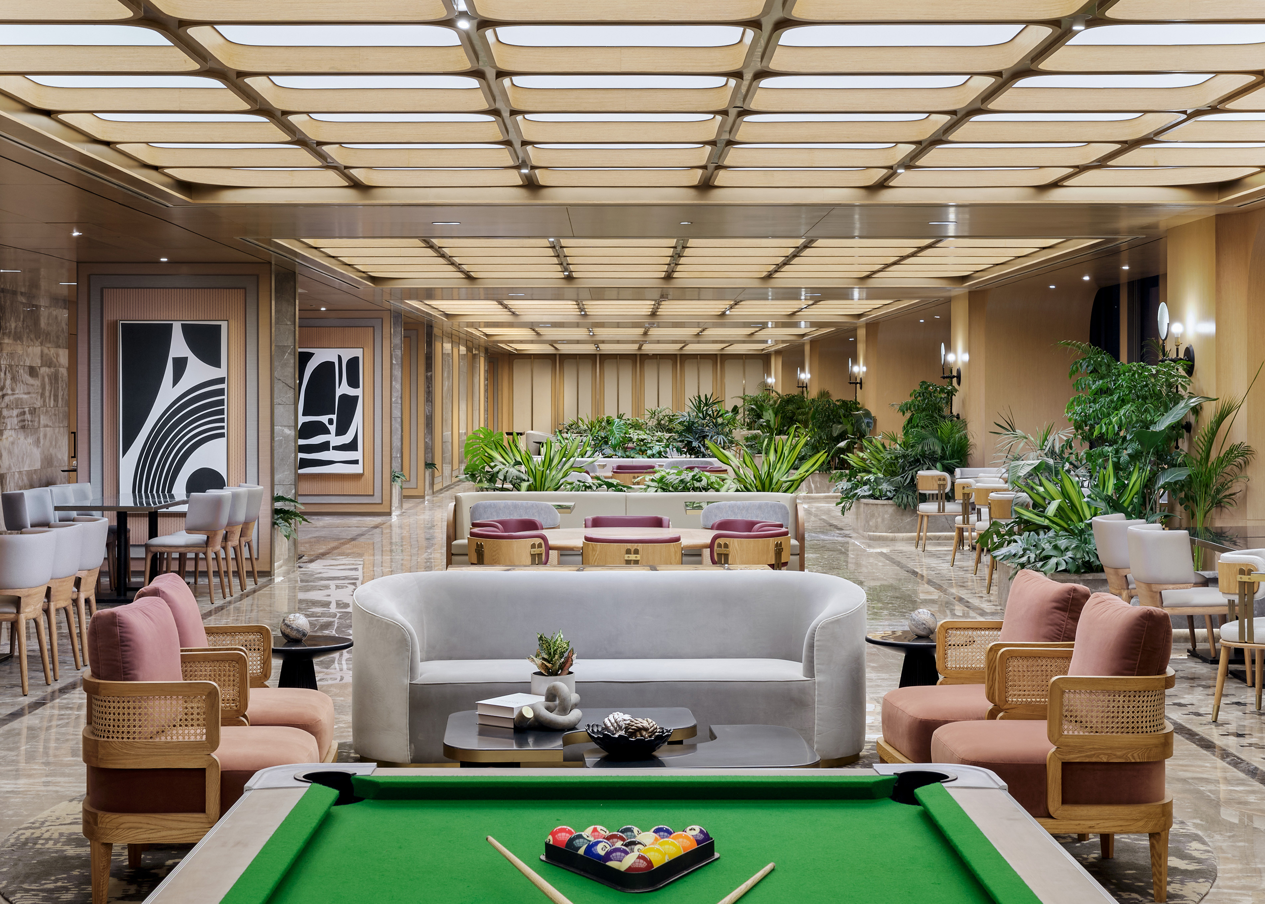 Luxurious lounge area with a pool table in the foreground. Cozy seating, modern art, and lush plants create an inviting, elegant atmosphere.