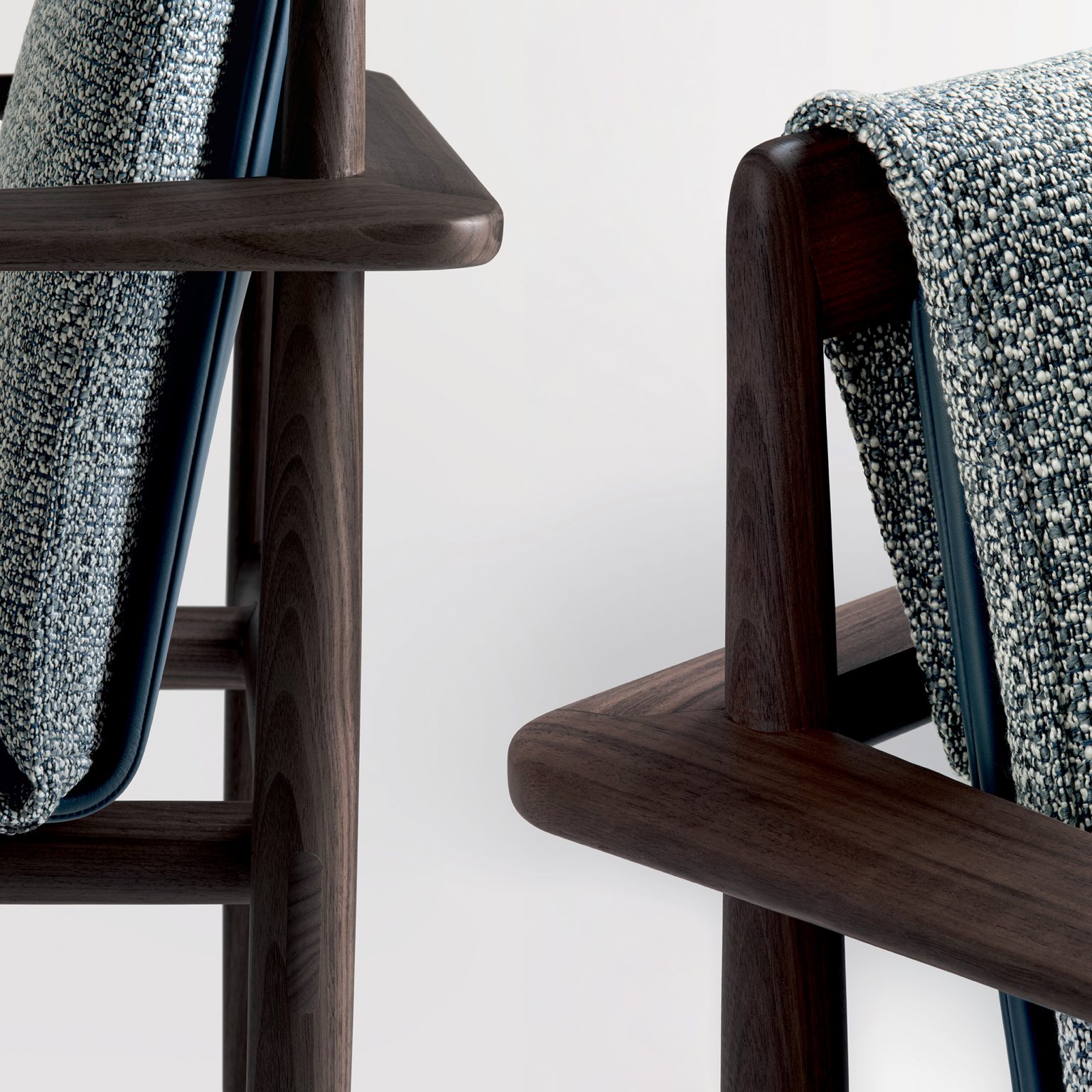 Close-up of Giorgetti - KUMIKI's chairs featuring dark wooden frames and textured blue-gray upholstery. The design conveys a sleek, modern aesthetic.