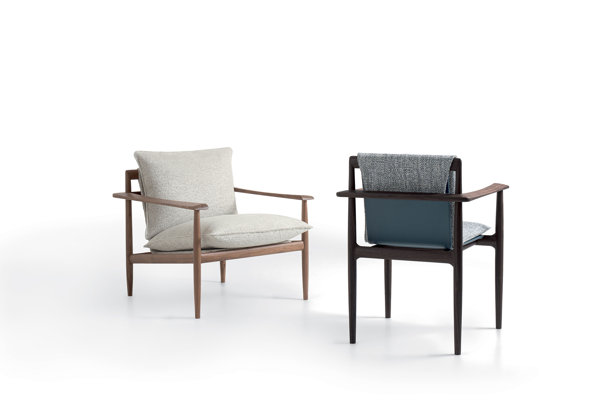 Two Giorgetti Kumiki armchairs on a white background. One has a beige cushion and light wood frame, the other, a dark frame with blue and gray upholstery. Sleek and minimalist design.