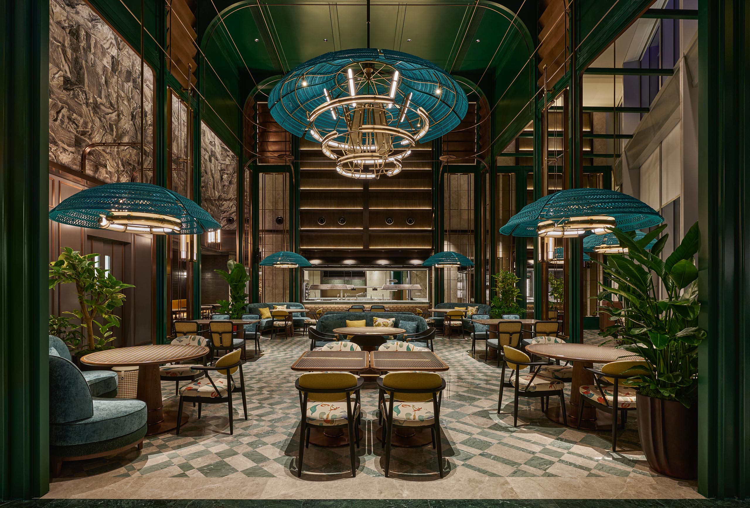 Spacious, elegant restaurant with high ceilings and large blue chandeliers. Greenery surrounds chic seating, creating a cozy, inviting atmosphere.
