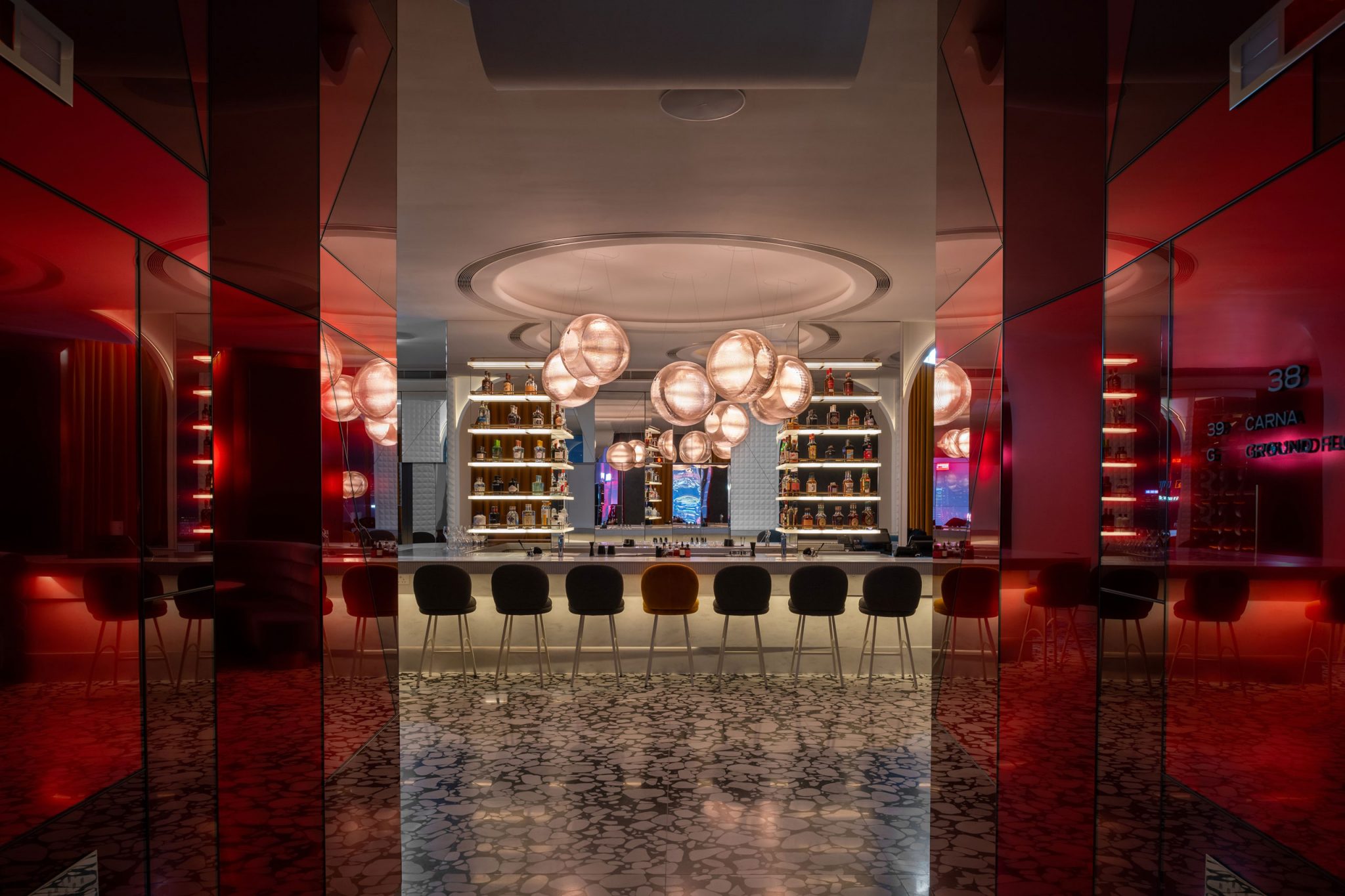 Stylish modern bar with circular pendant lights, marble floor, and red accents. High chairs line the bar, creating a sleek, inviting ambiance.